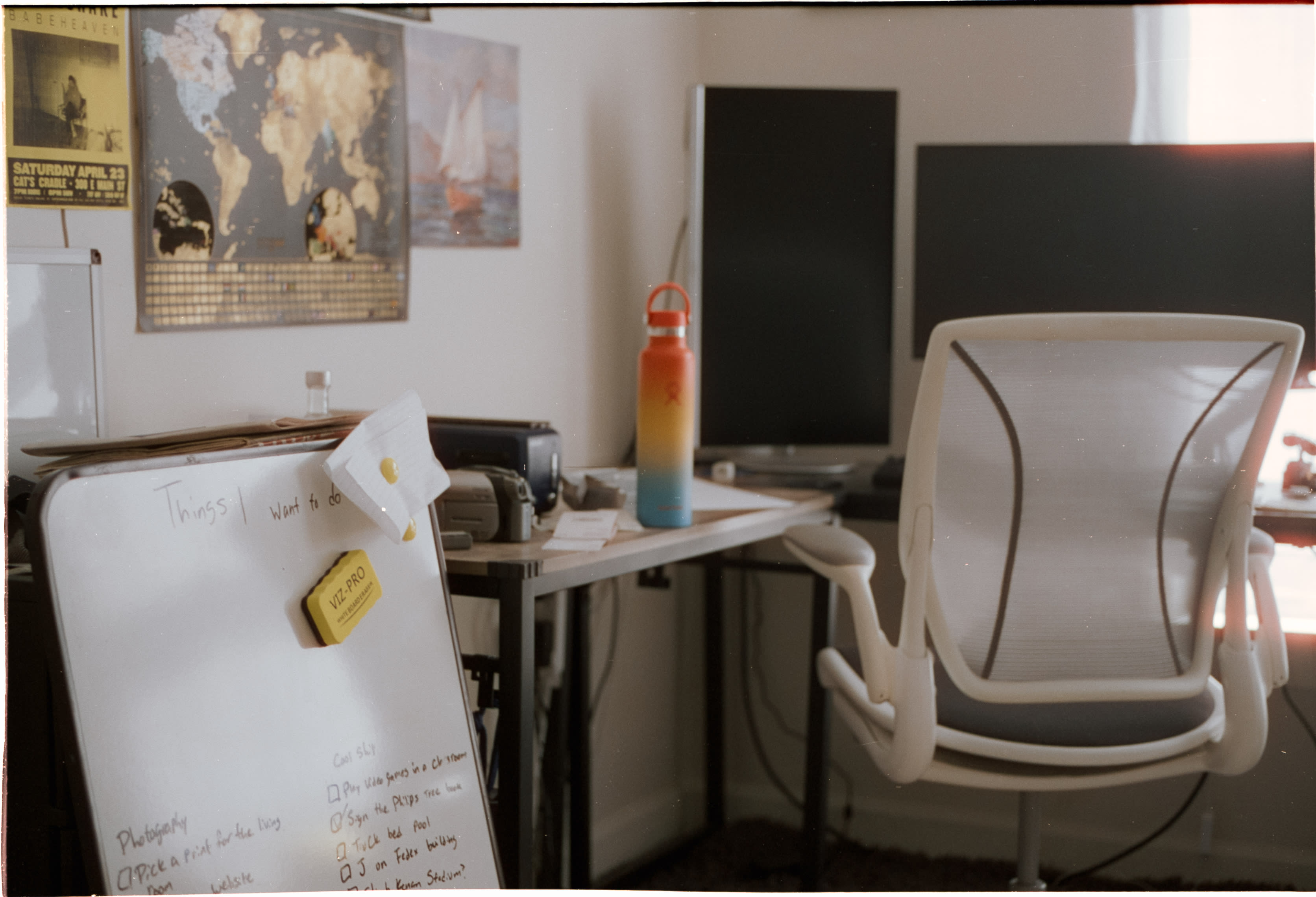 A desk with two monitors and an office chair below a world map