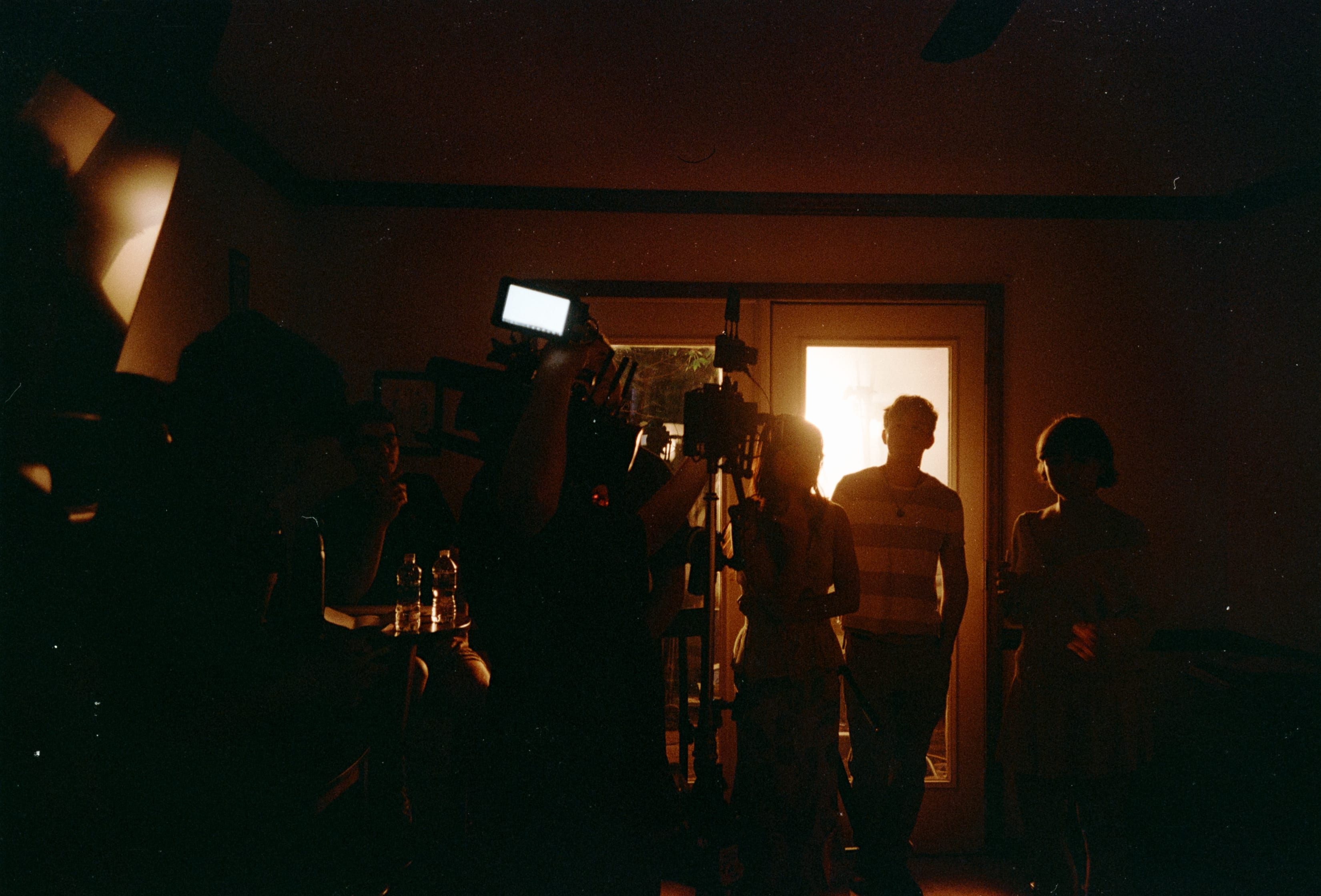 The crew silhouetted around a camera in a doorway lit orange