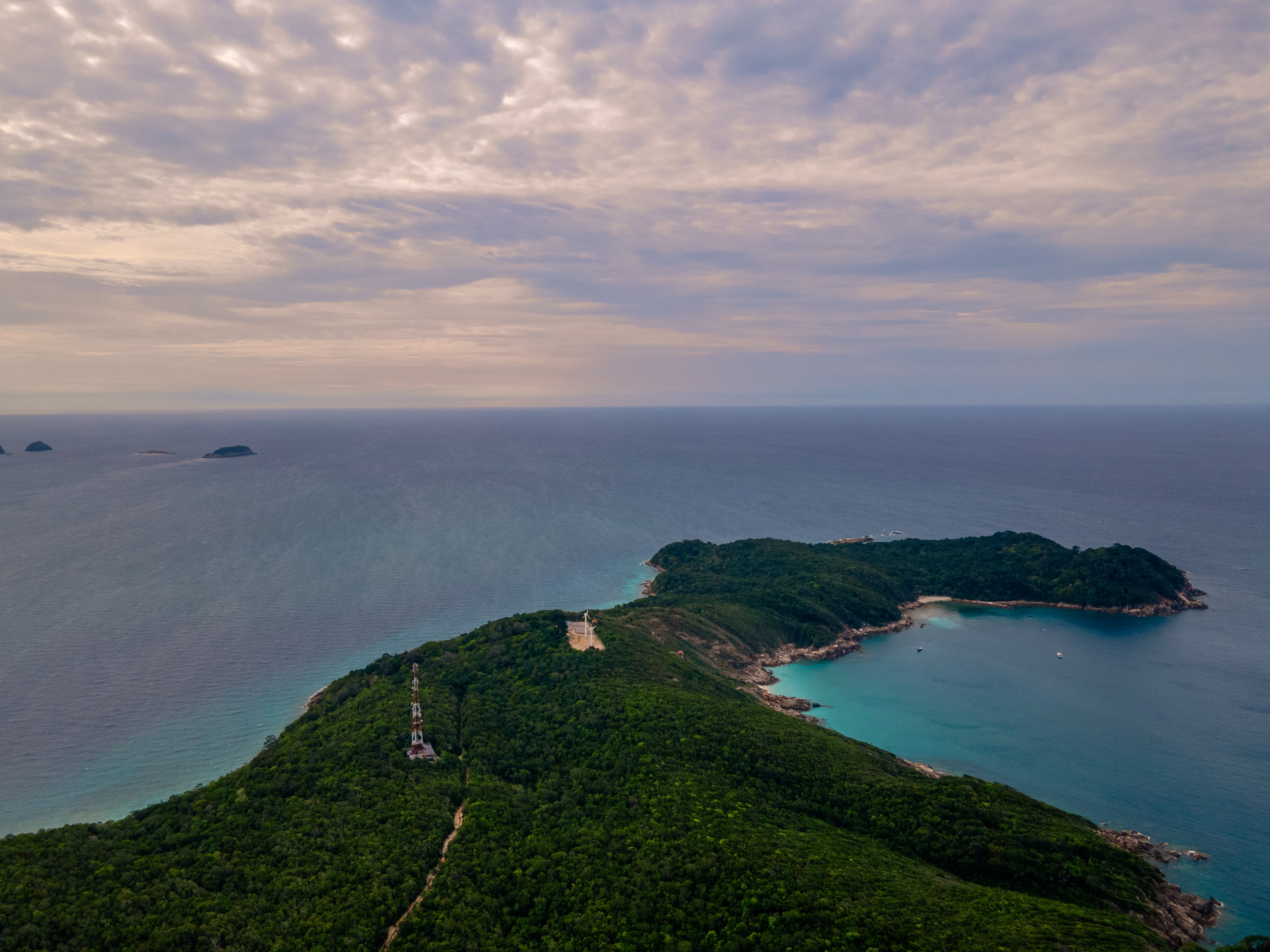 A forested headland with a tower on its ridge, reaching into the sea under a cloudy sky