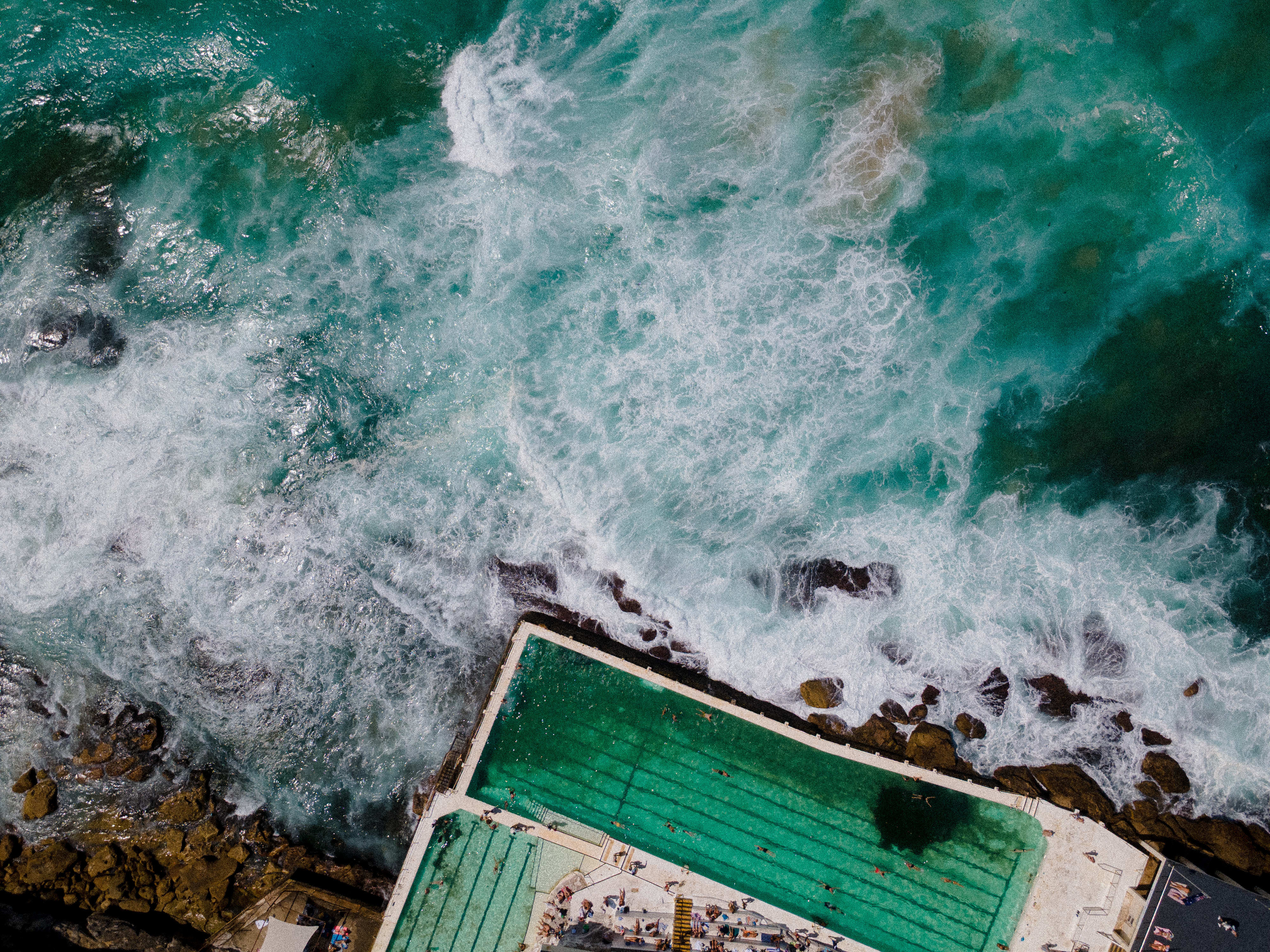 Surf churning over the rocks beside the Bondi Icebergs pool, seen from above