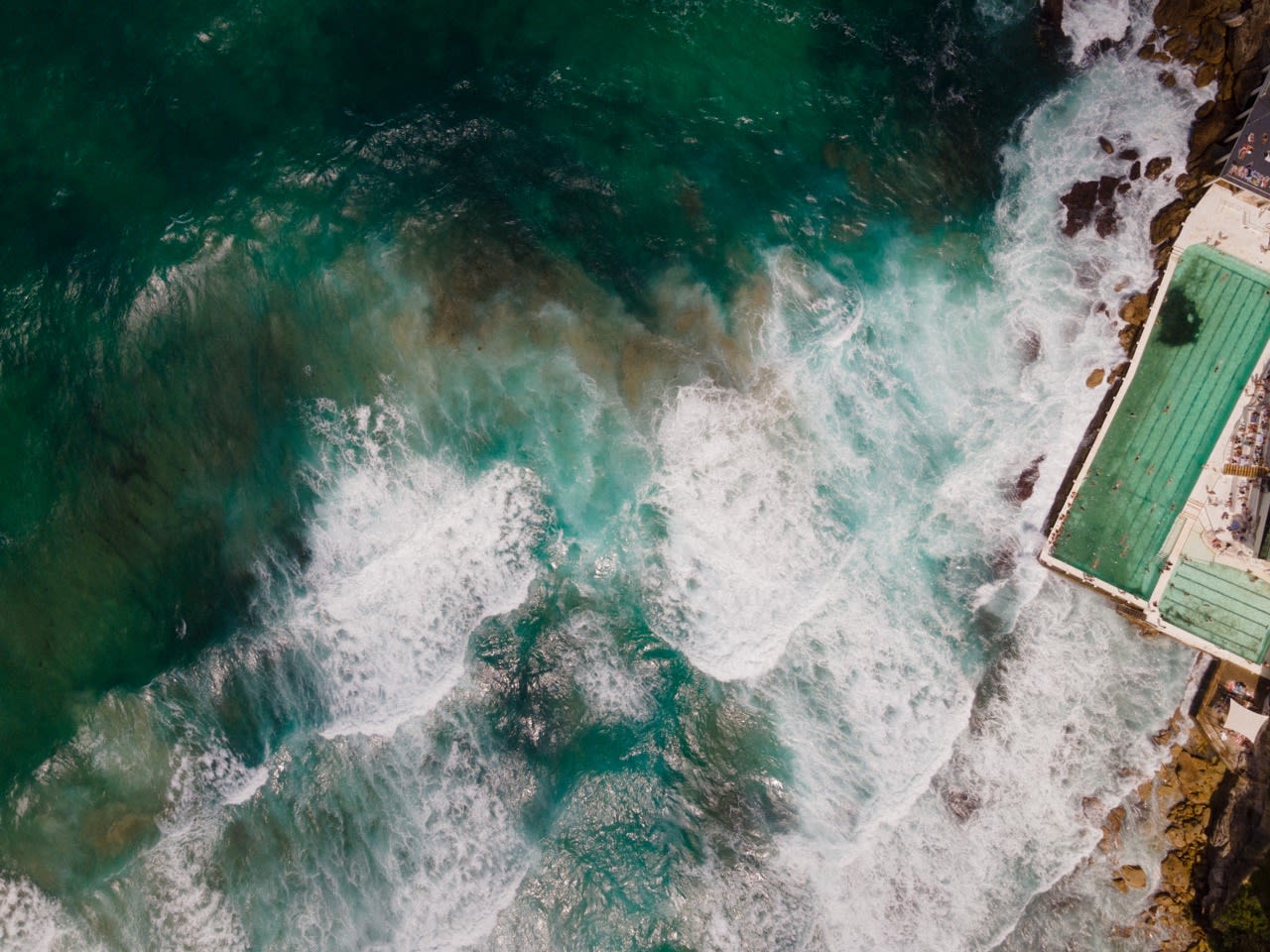 Waves rolling in toward the Bondi Icebergs pool at the edge of the cliffs, seen from above