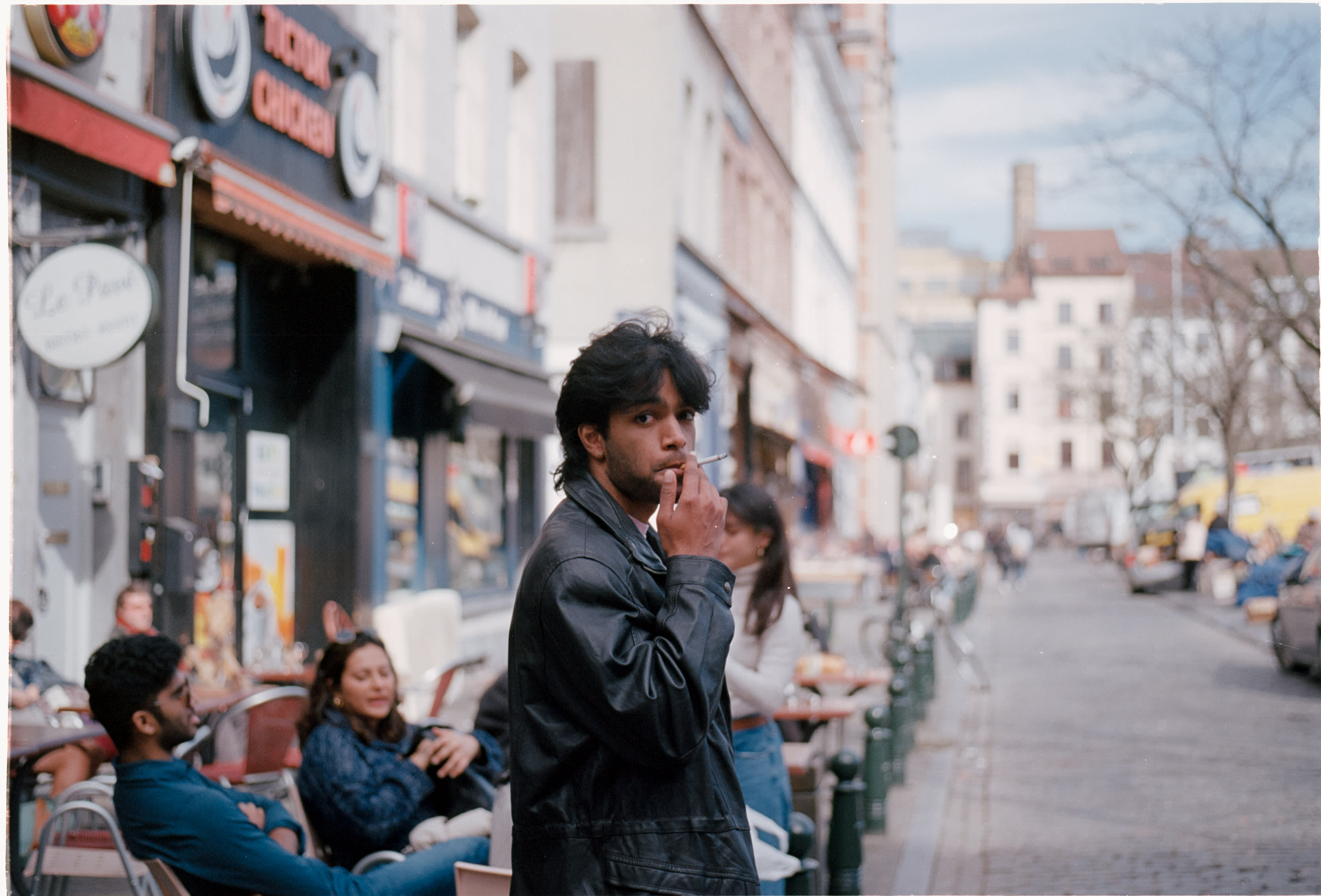 A friend smoking on a café-lined street while others sit outside