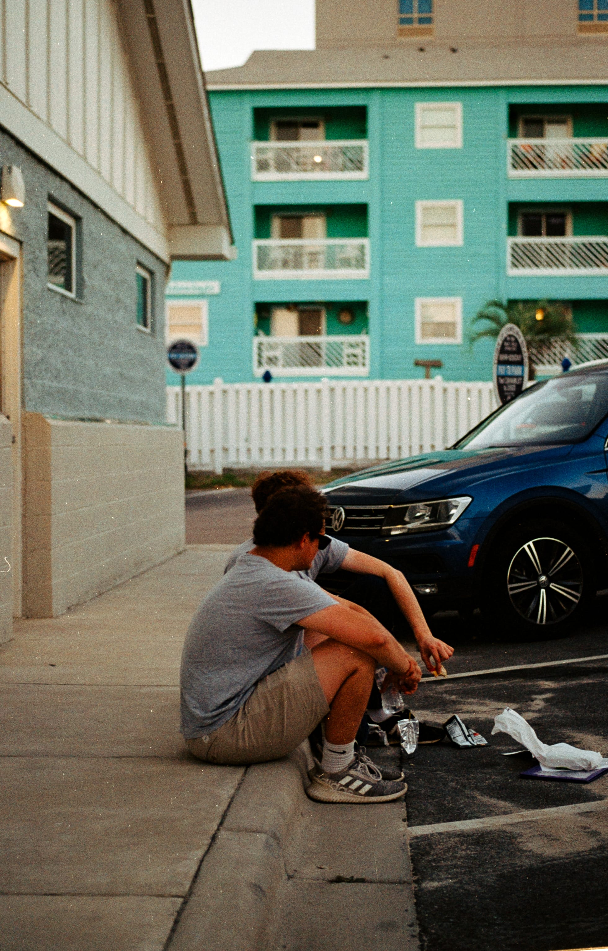 Two crew members sitting on a curb beside a teal beach hotel