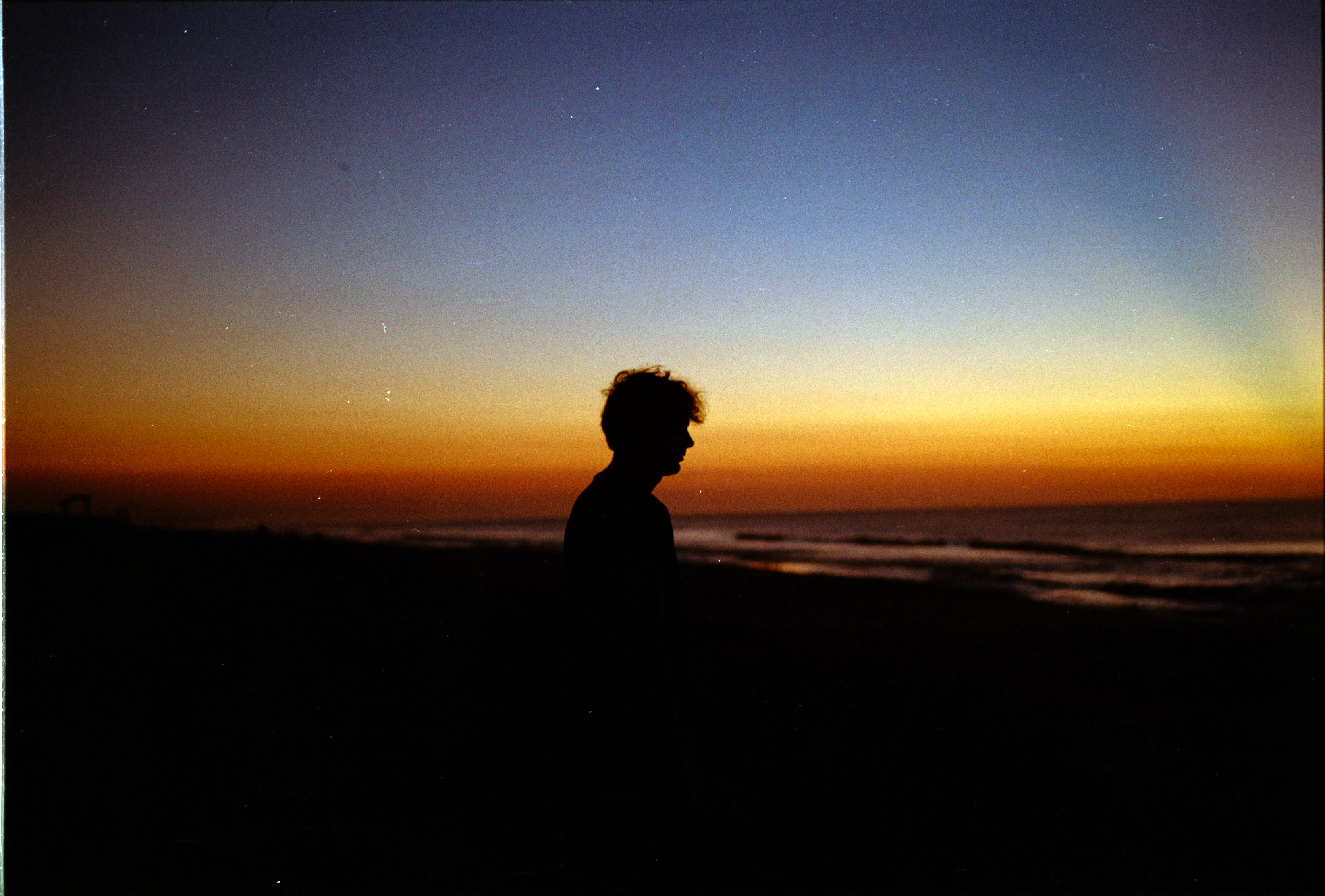 A lone silhouette against an orange and blue sunset over the ocean
