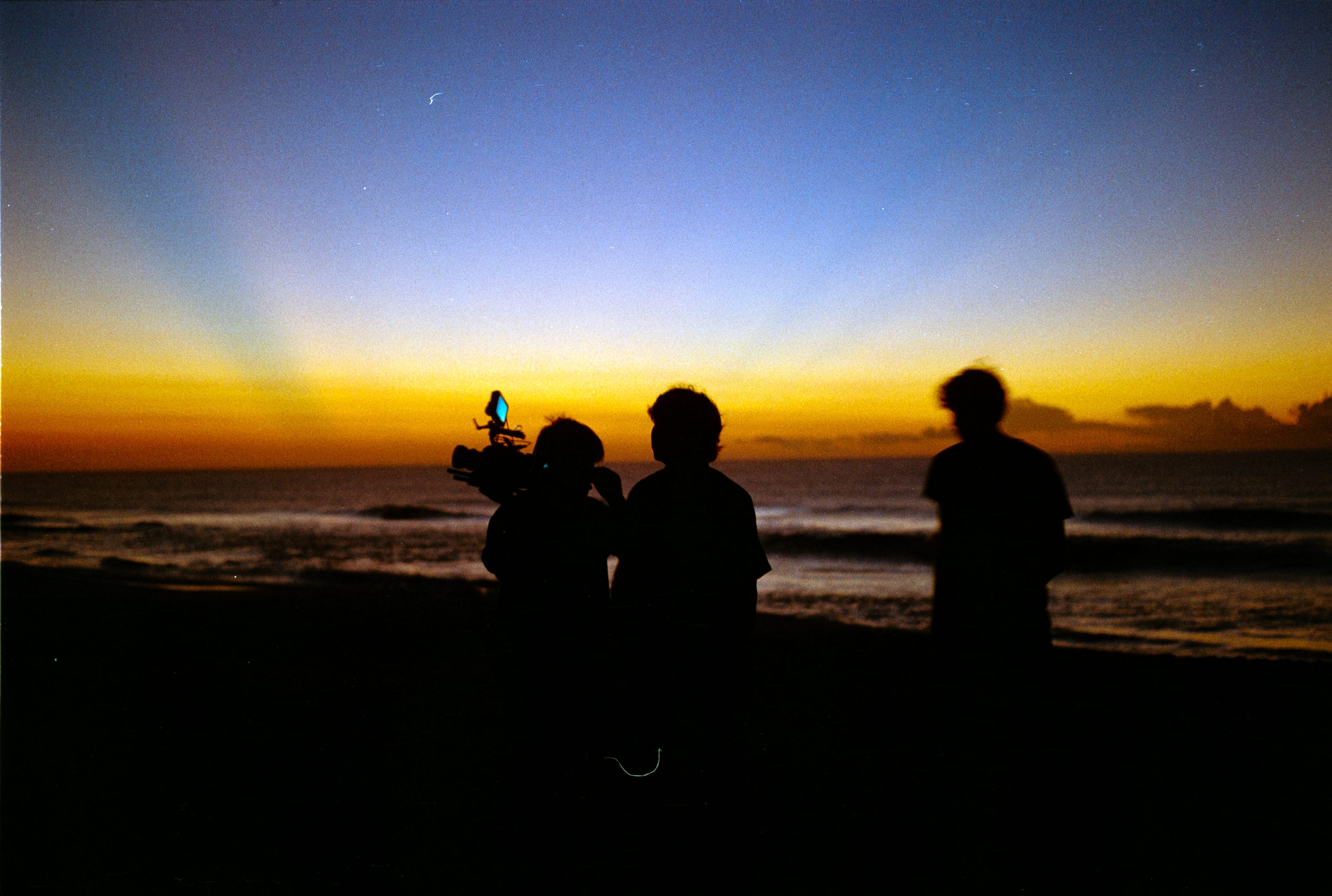 The crew silhouetted with a camera rig against a sunset over the ocean