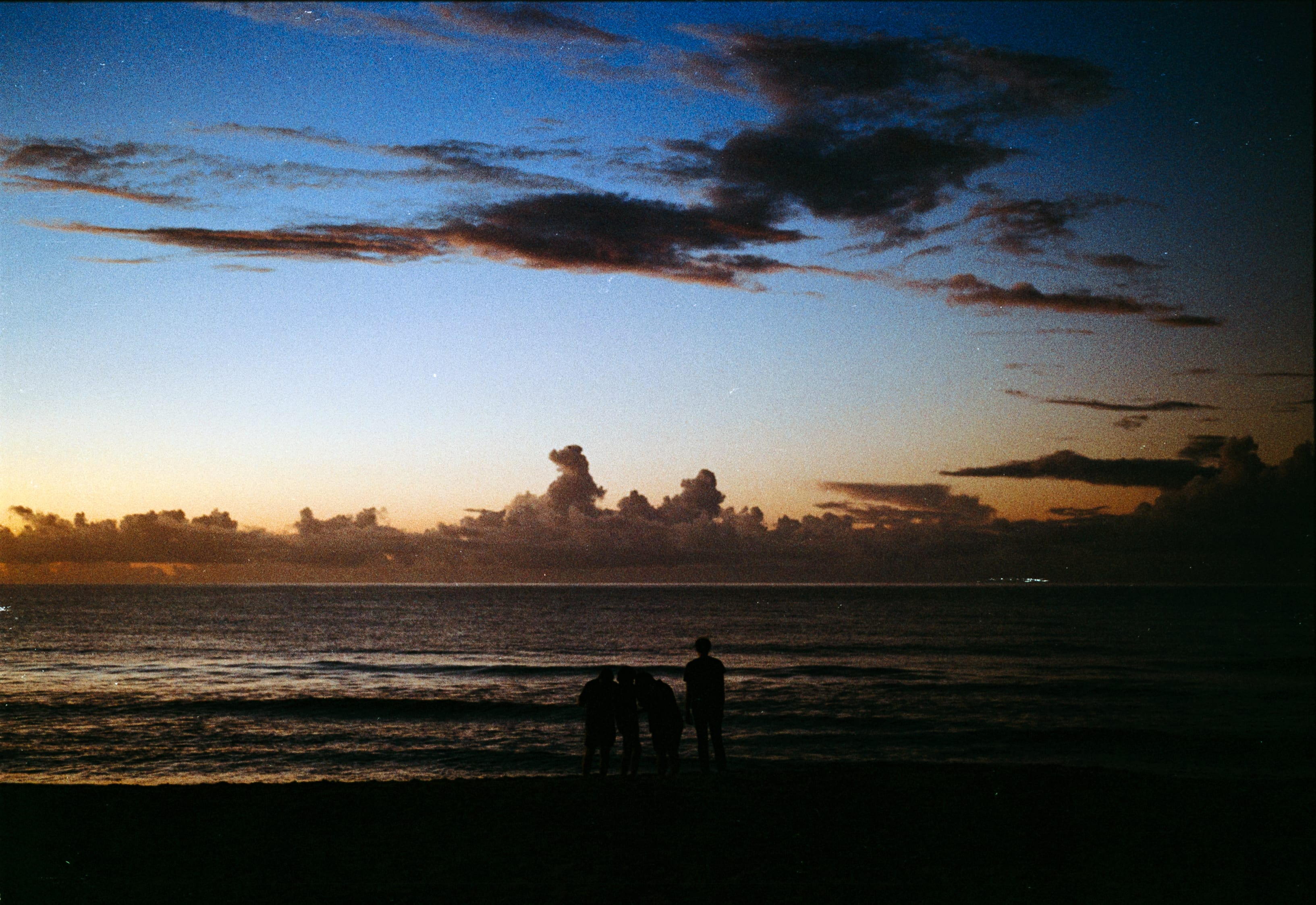 Small figures at the water's edge under dark clouds at dusk