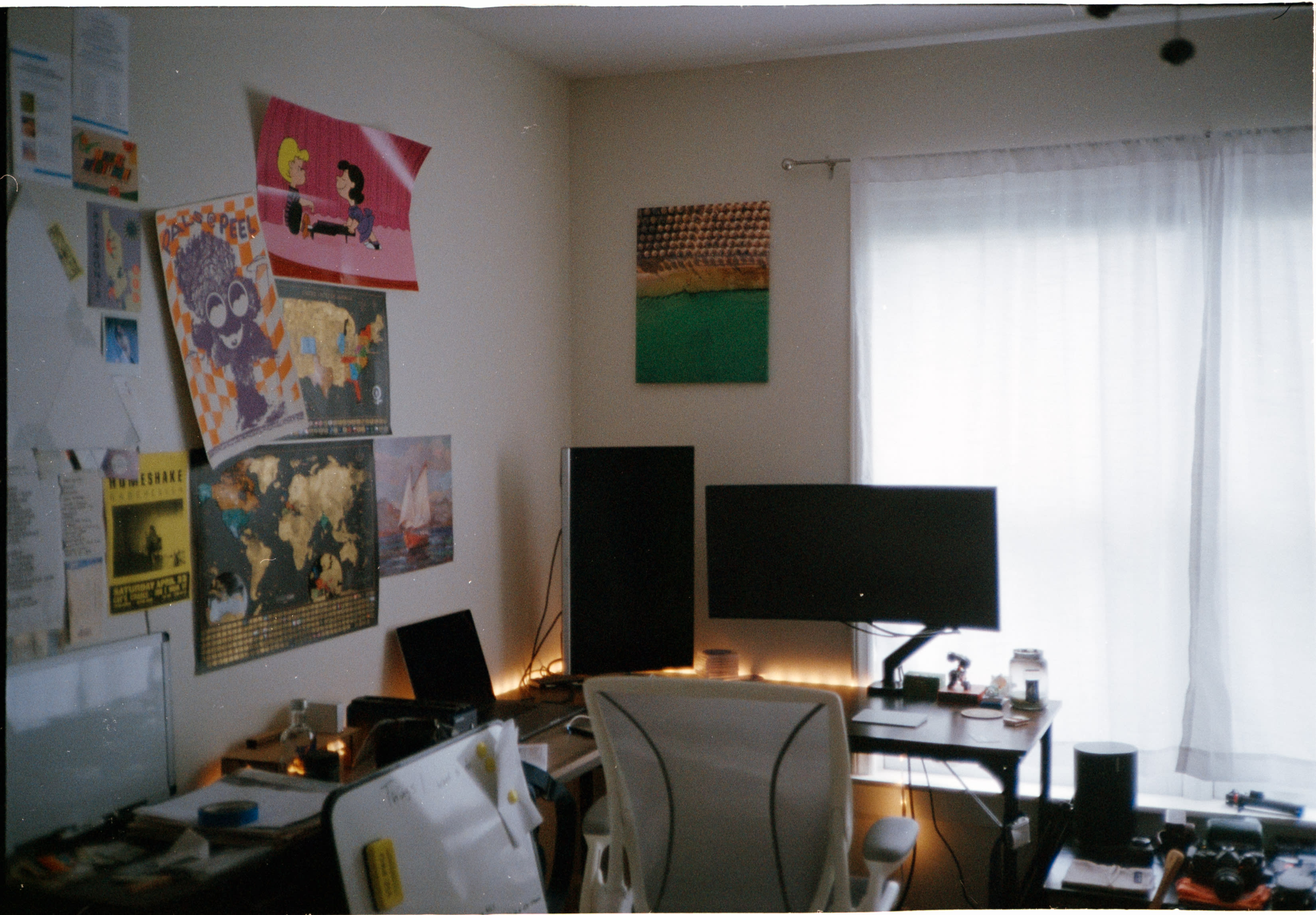 A desk with monitors and maps on the wall, lit by string lights