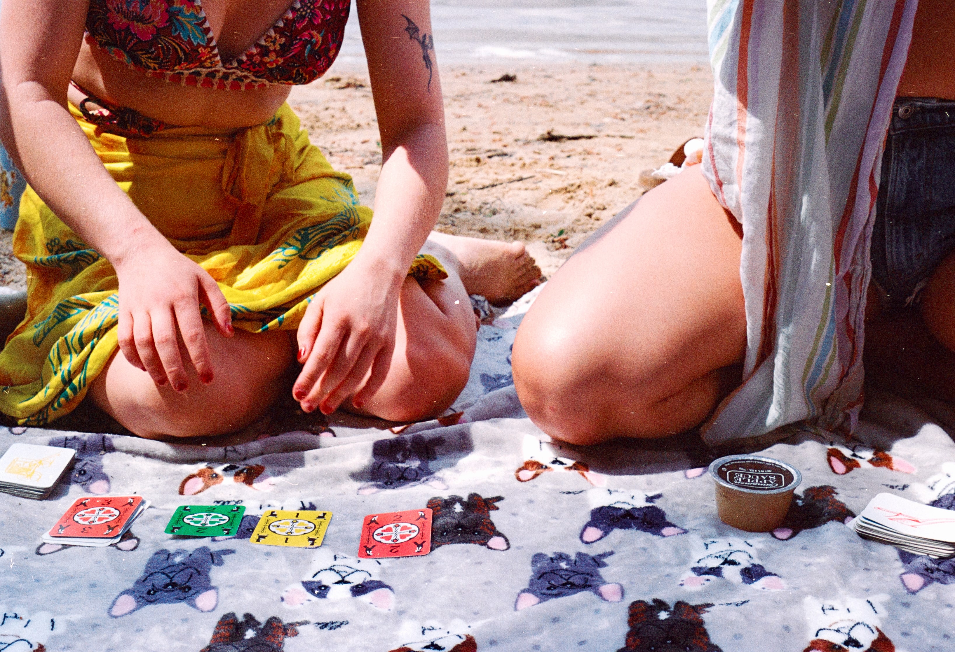 Two people kneeling on a beach blanket with a card game laid out