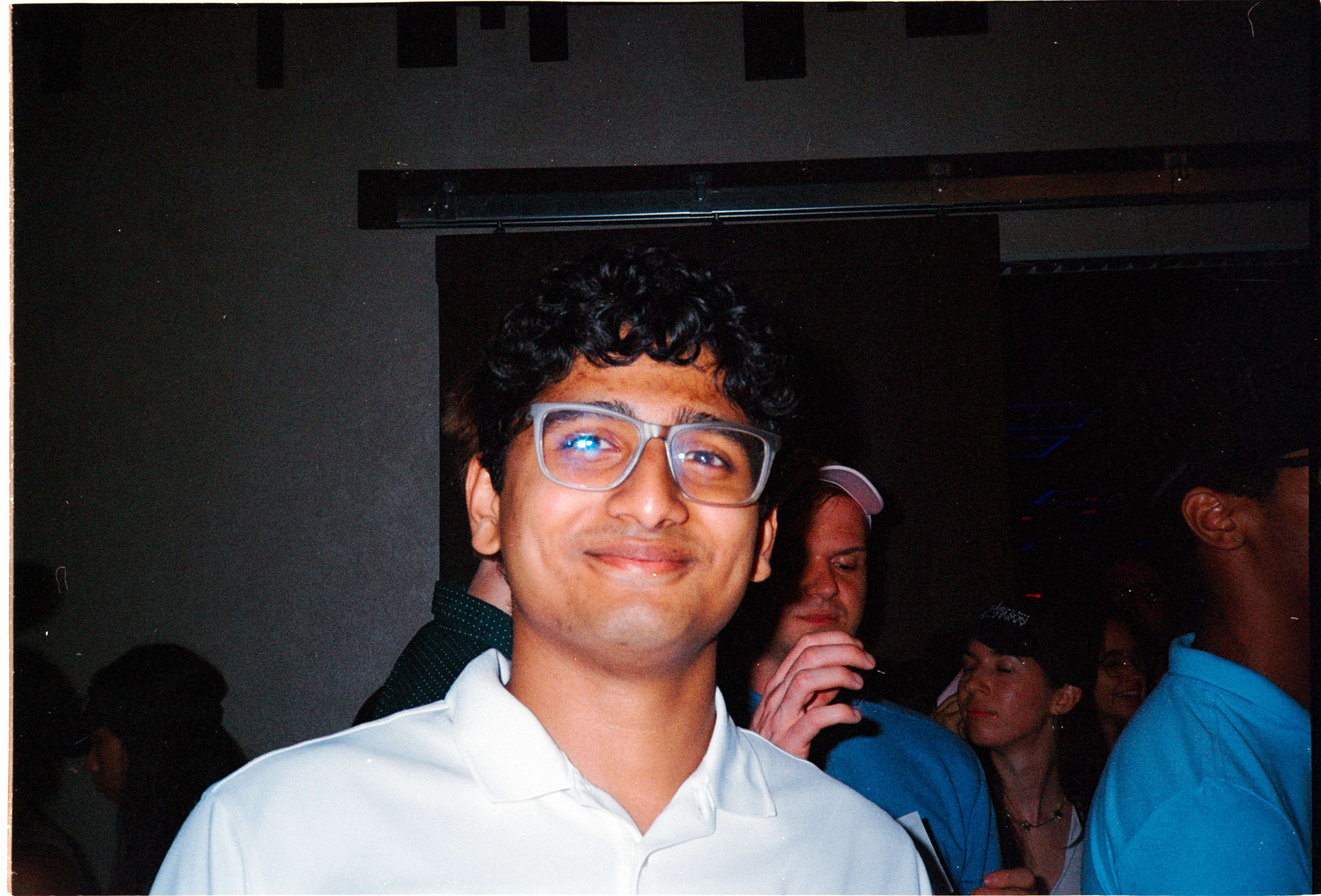 A friend in glasses smiling into the flash at a crowded party