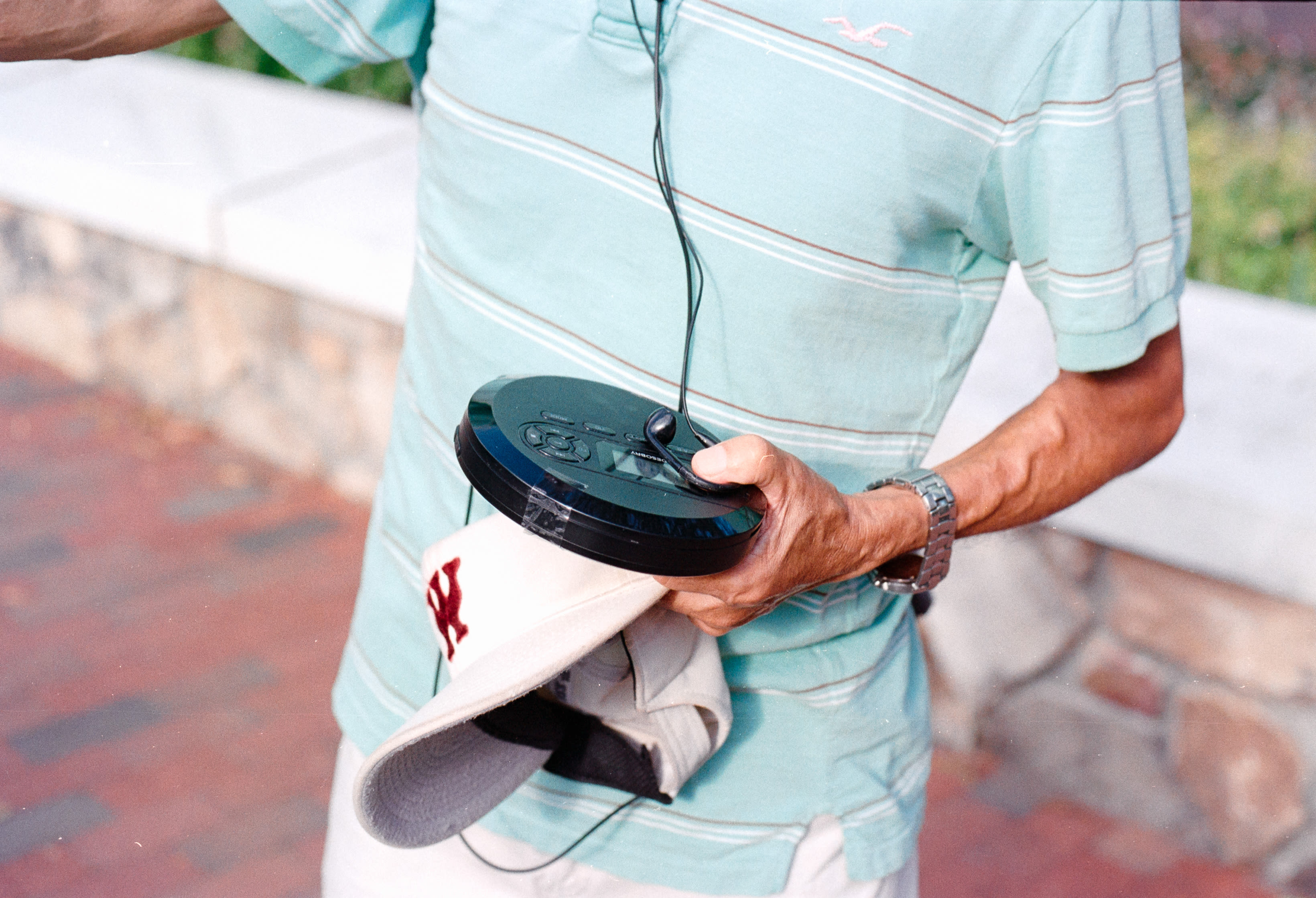 Someone holding a portable CD player and a cap behind their back