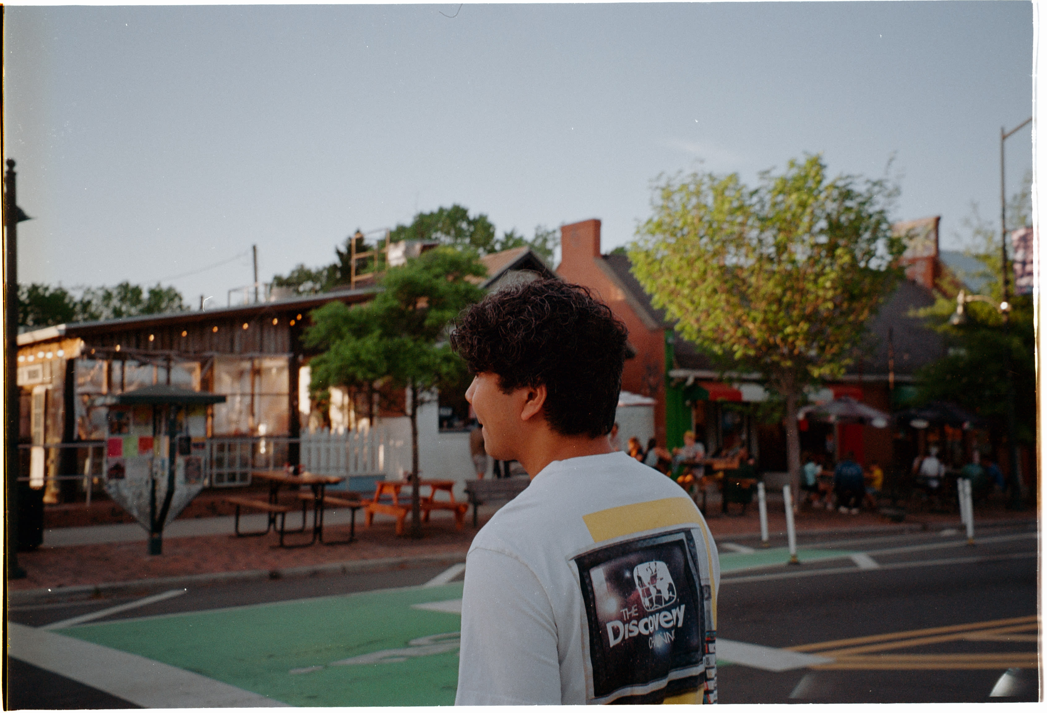 A friend in a graphic tee looking across the street at a restaurant patio at dusk