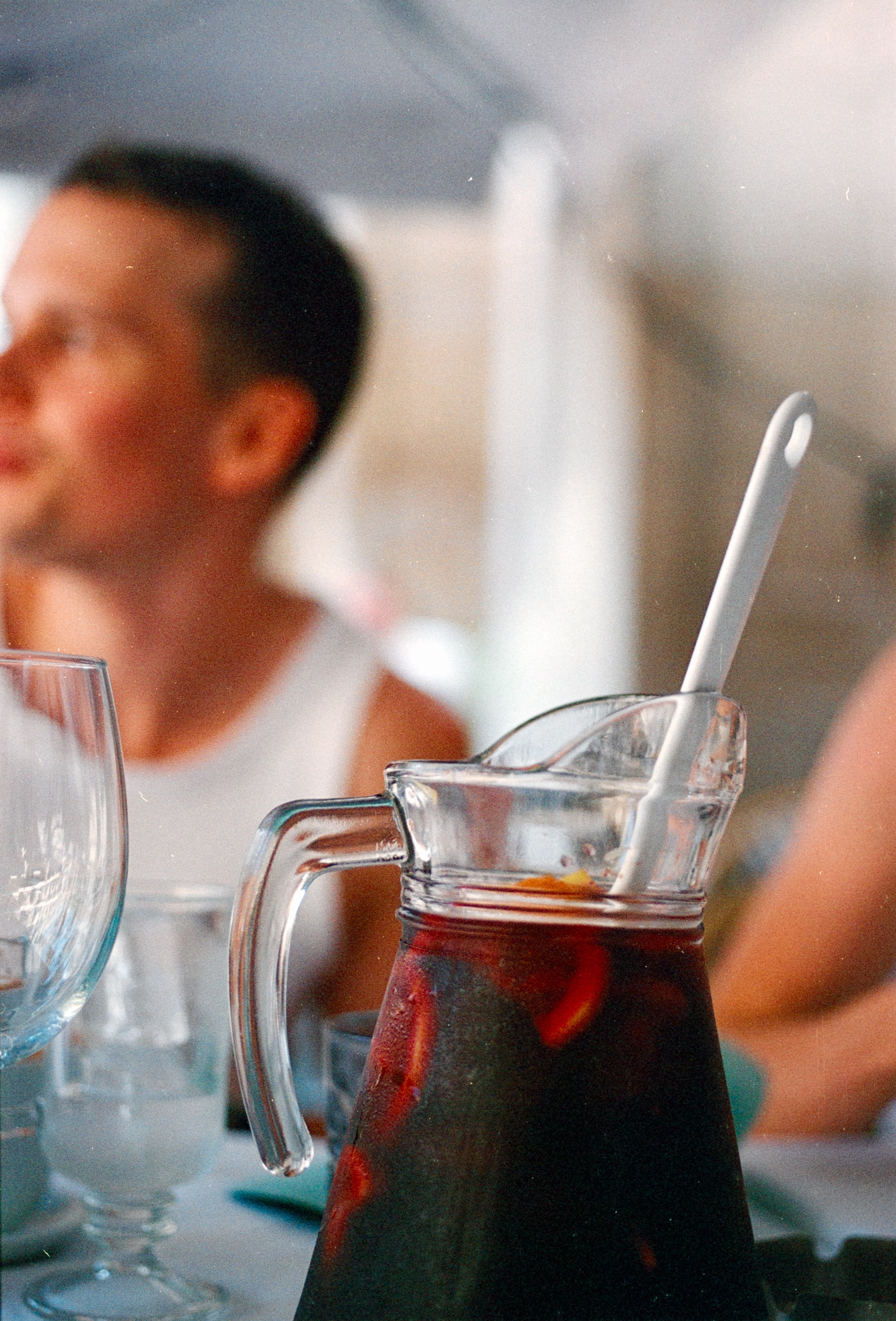 A pitcher of sangria on a table, with a friend behind it