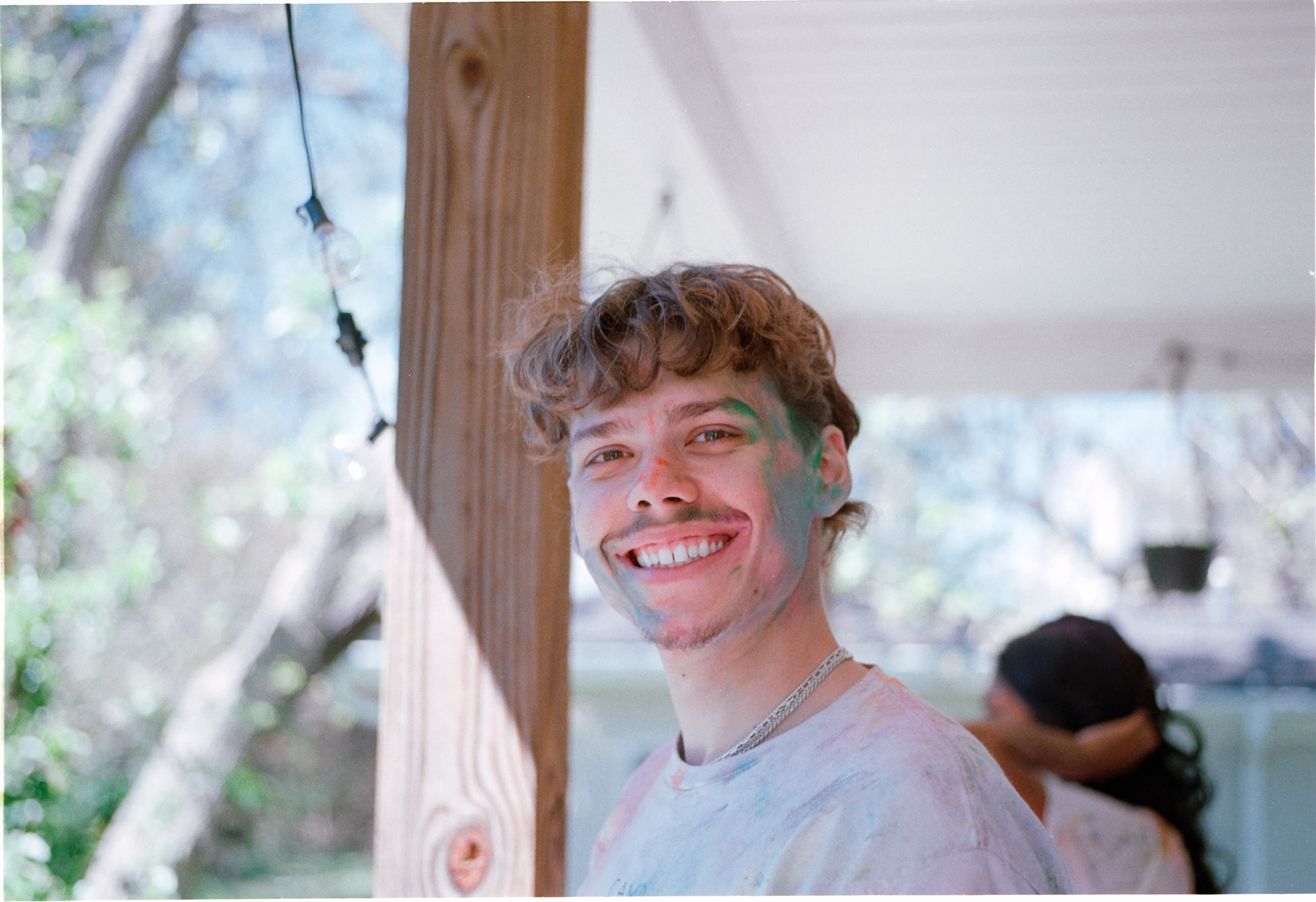 A friend dusted in colored powder, smiling on a porch