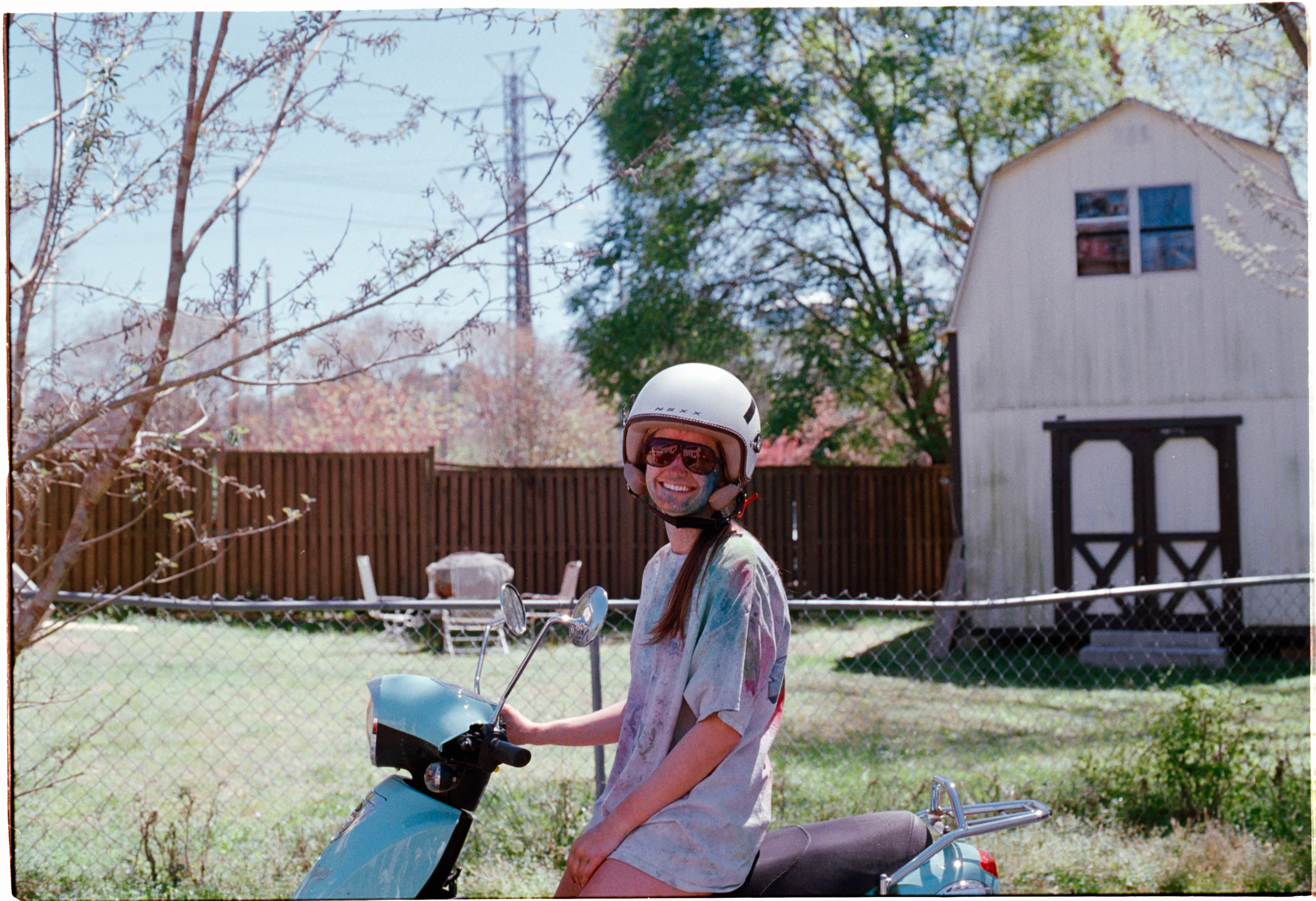 A friend in a helmet on a blue scooter in a backyard