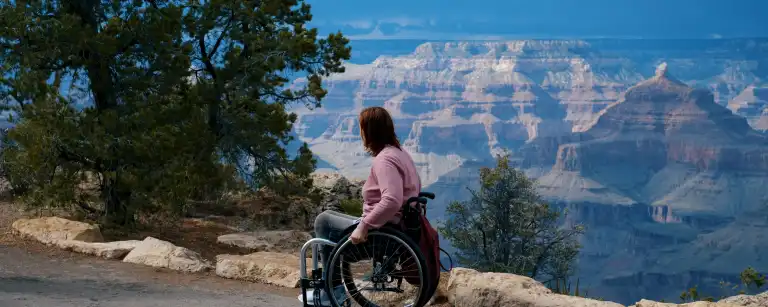 a woman in a wheel chair, on the side of the road, overlooking Grand Canyon