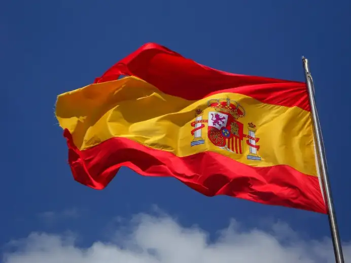 a spanish flag waving in the wind with clear blue skies behind it