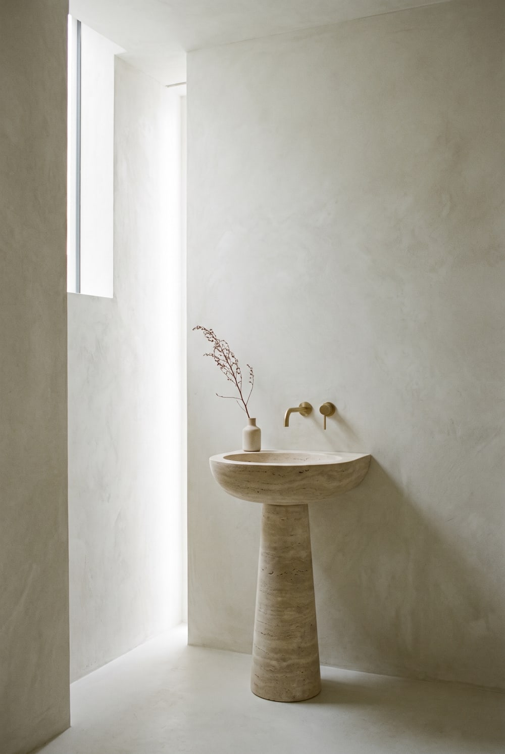 A sculptural stone pedestal basin against a pale limewash wall.
