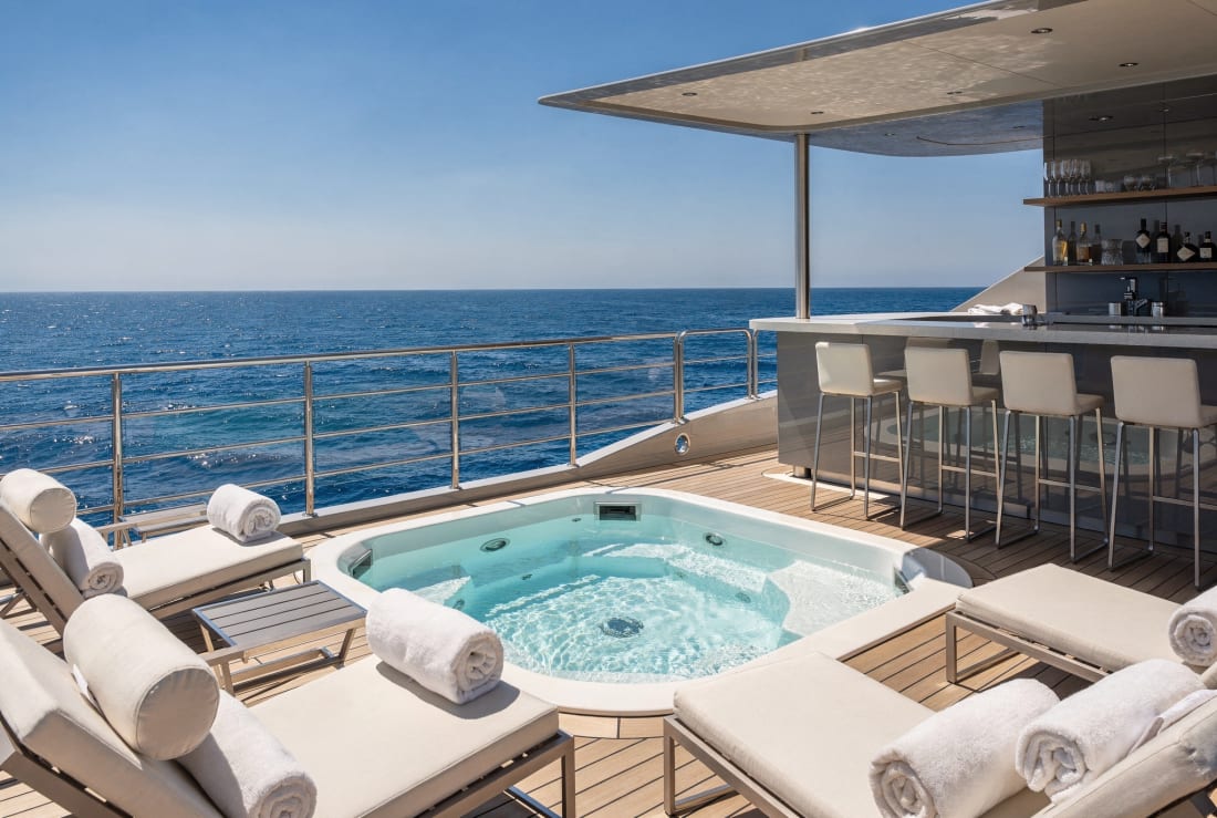 A sun deck with a jacuzzi and loungers under a bright sky.