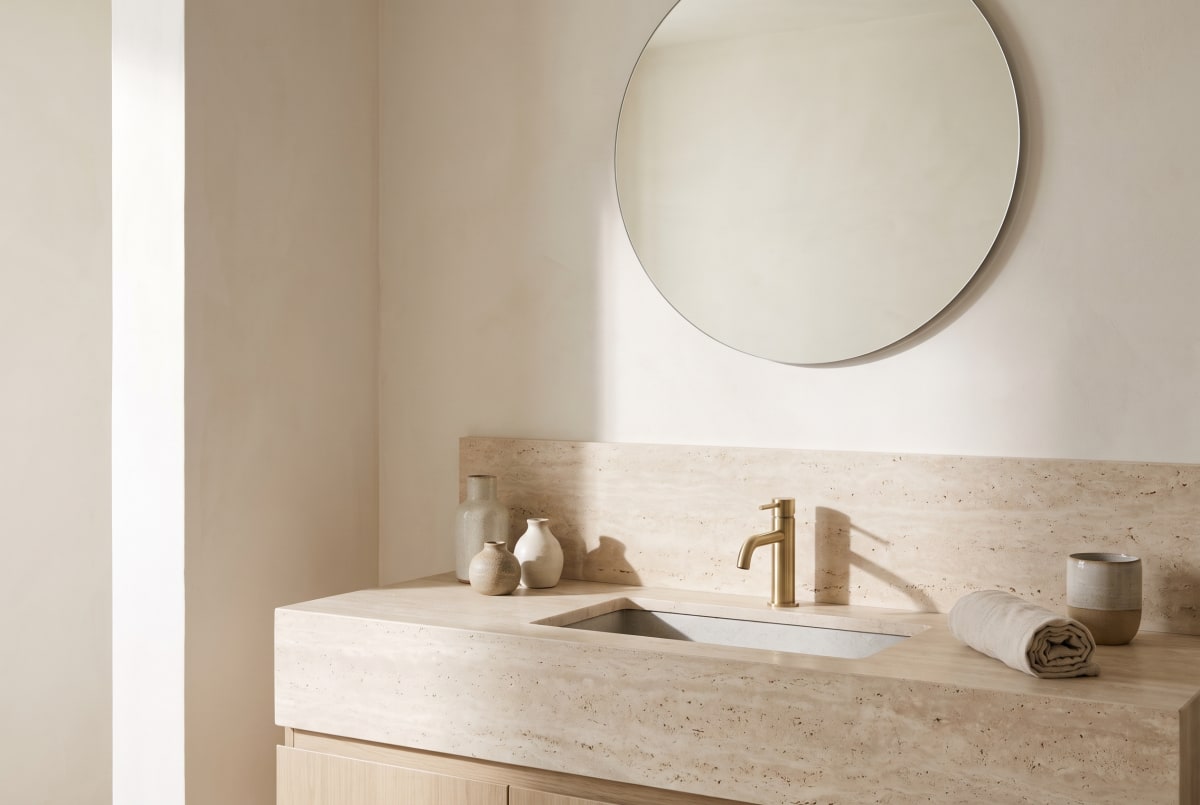 A travertine vanity with an undermount stone basin and brushed-brass tap.