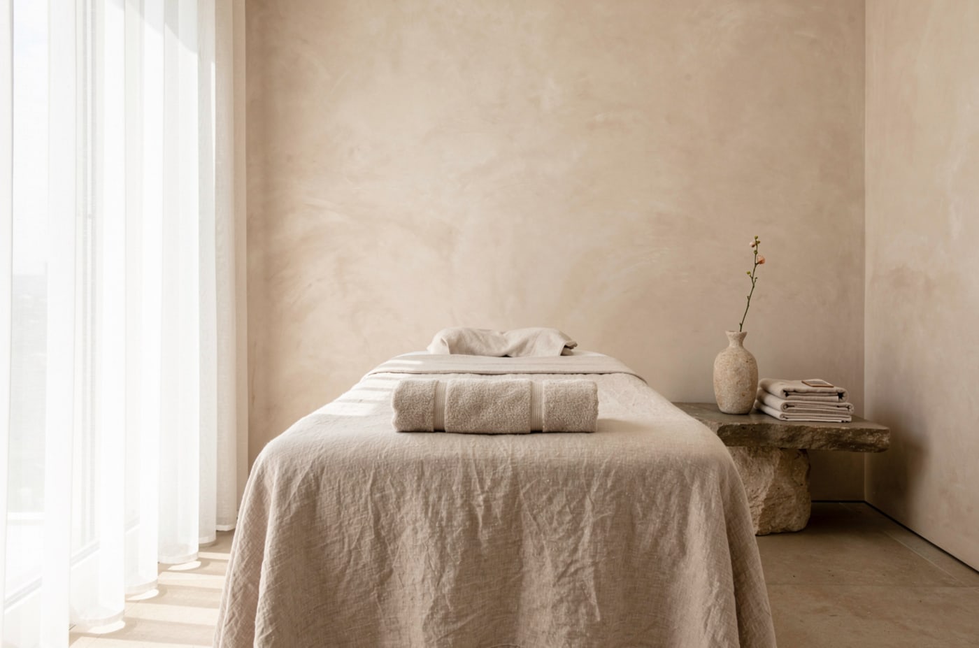 STILLA — a calm, linen-dressed spa treatment room in soft daylight.