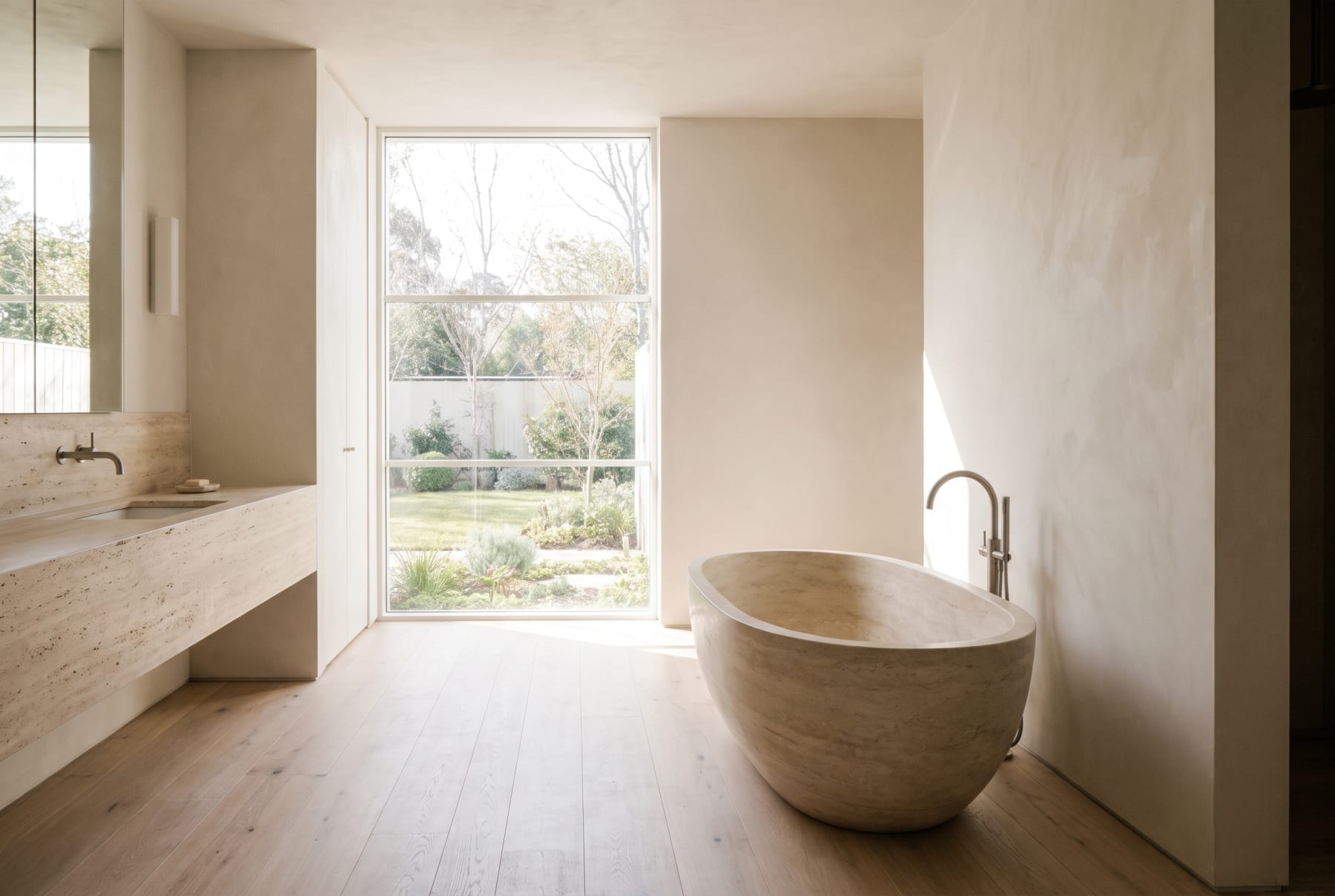 A calm, light-filled ensuite with a freestanding bath and travertine vanity.