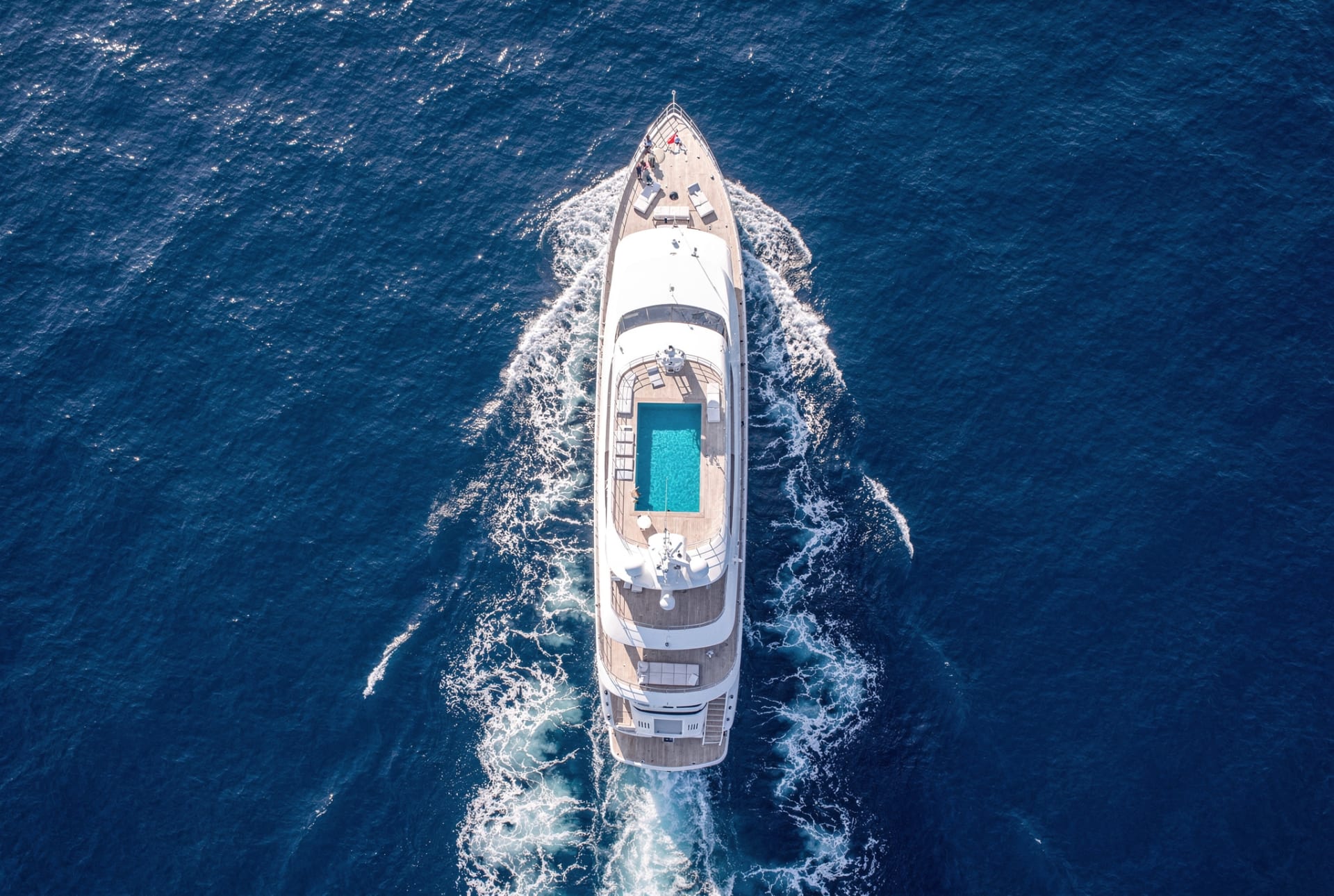 A superyacht carving a wake across deep blue open water, seen from above.