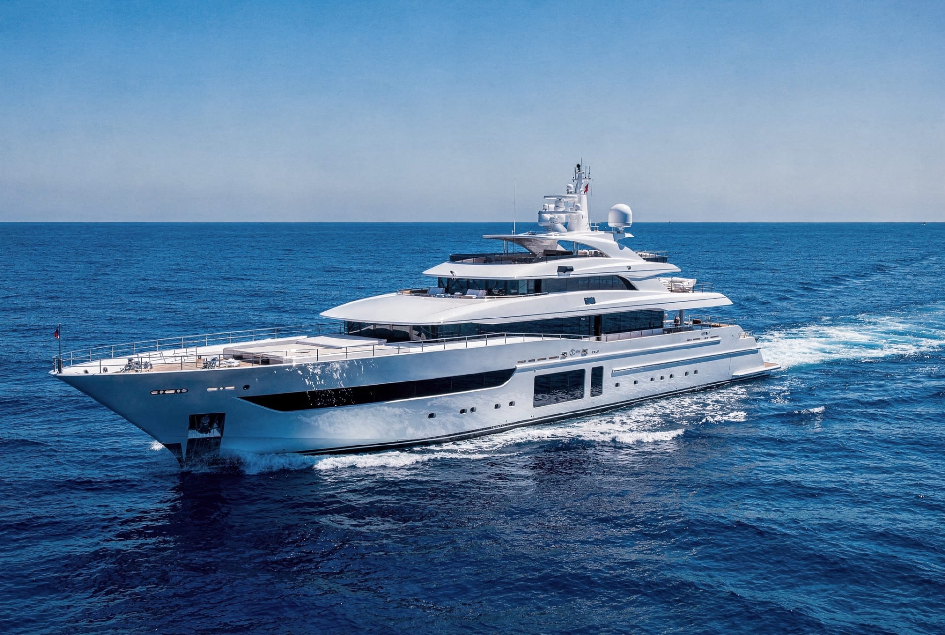 A modern motor superyacht cruising on a deep blue sea under a bright sky.