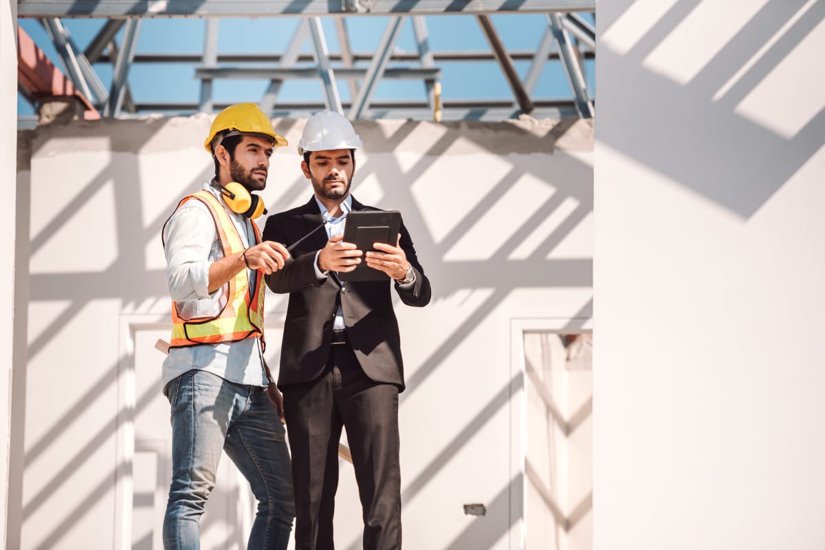 Ingeniero civil y jefe de obra revisando planos y tablet digital en obra de construcción