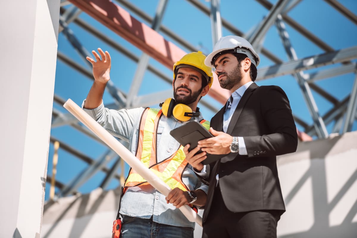 Ingeniero civil y jefe de obra revisando planos digitales en tablet en obra de construcción