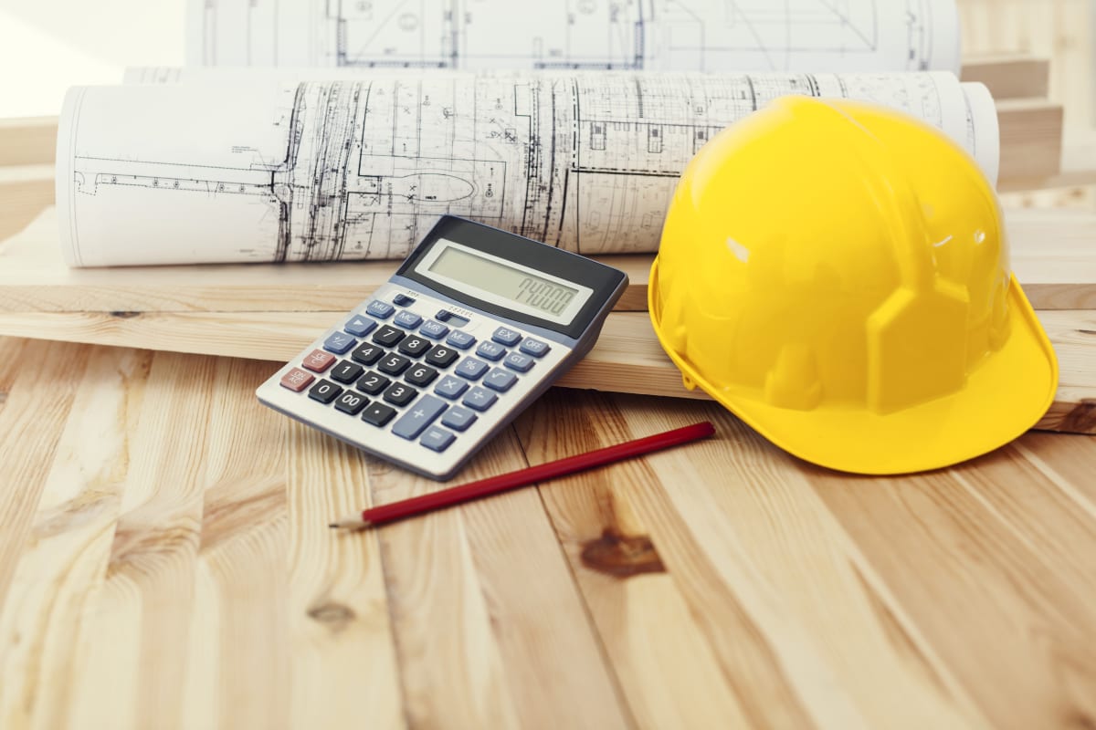 Casco amarillo con planos y calculadora sobre una mesa de madera