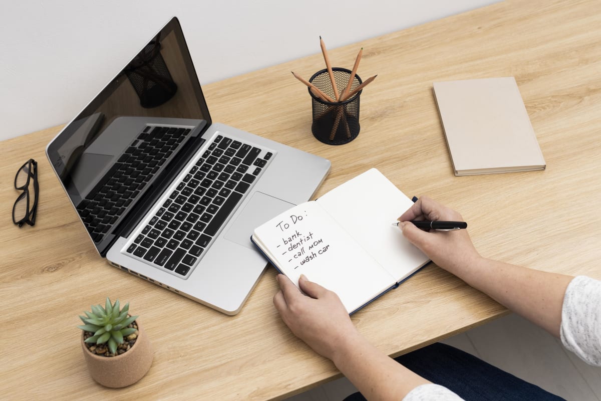 Cuaderno con lista de tareas junto a un laptop sobre un escritorio