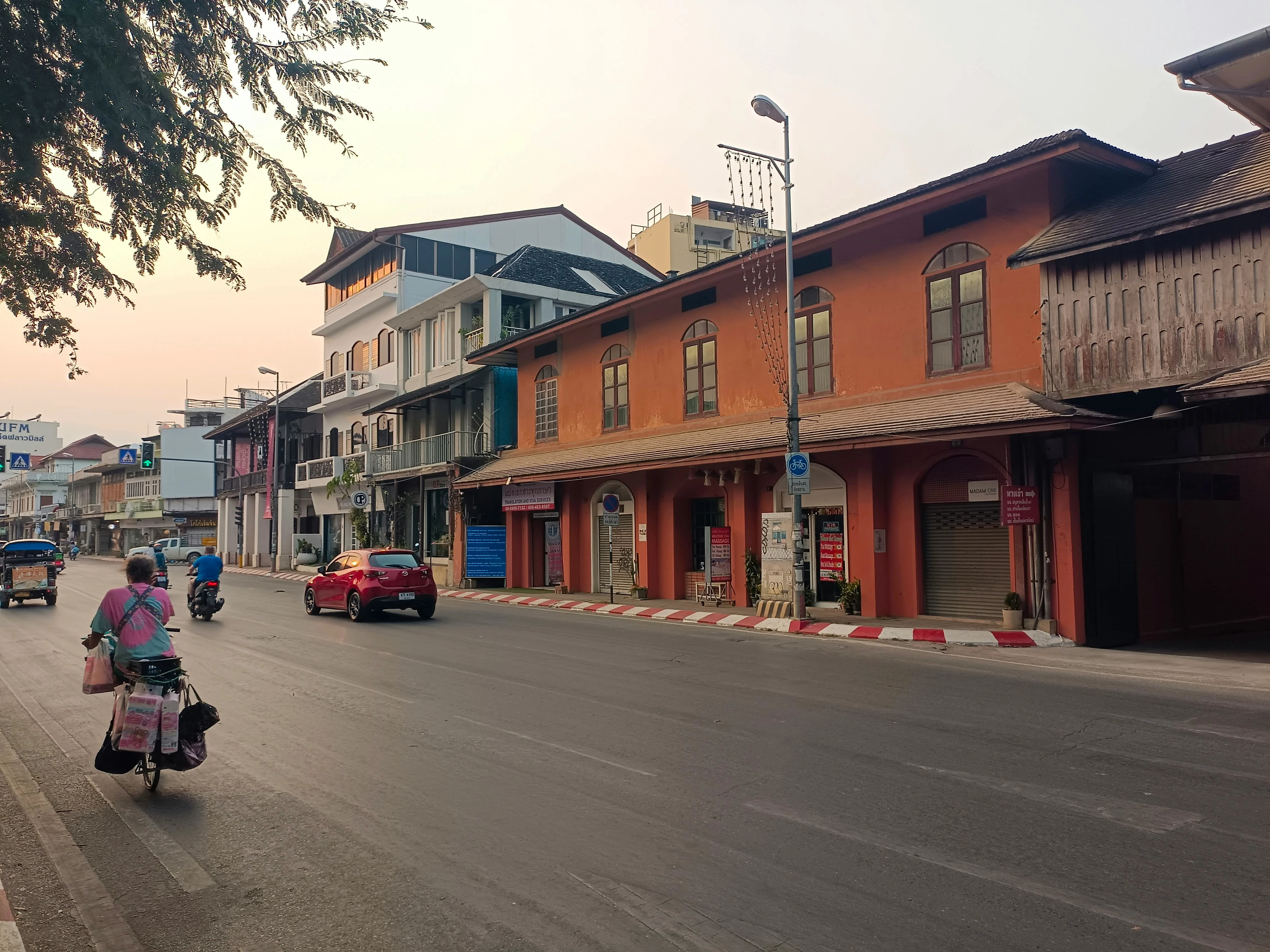 A lively street in Chiang Mai with people and vehicles under the soft evening light. More info Share