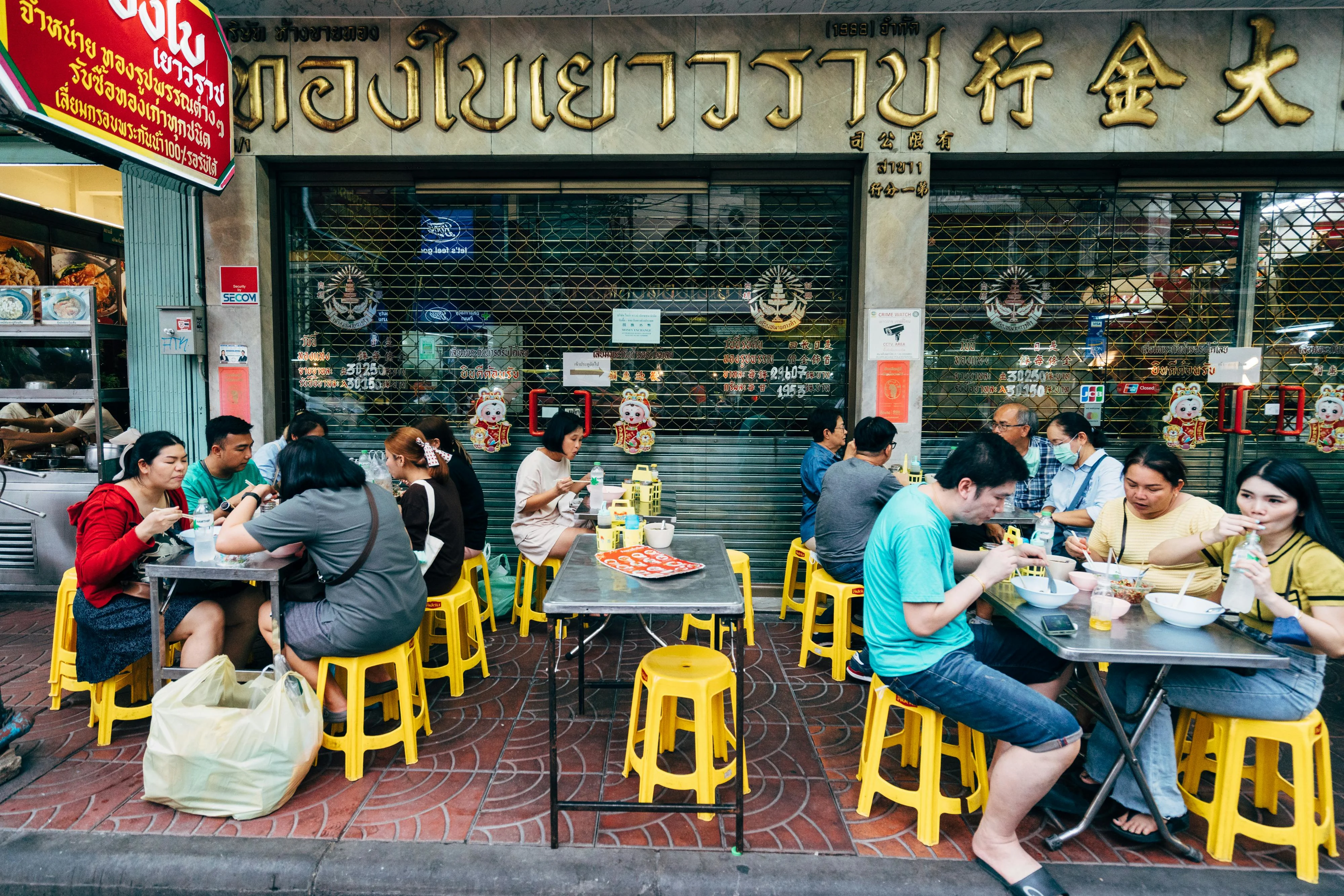 People enjoying authentic Thai street food at outdoor tables in Bangkok city. More info Share