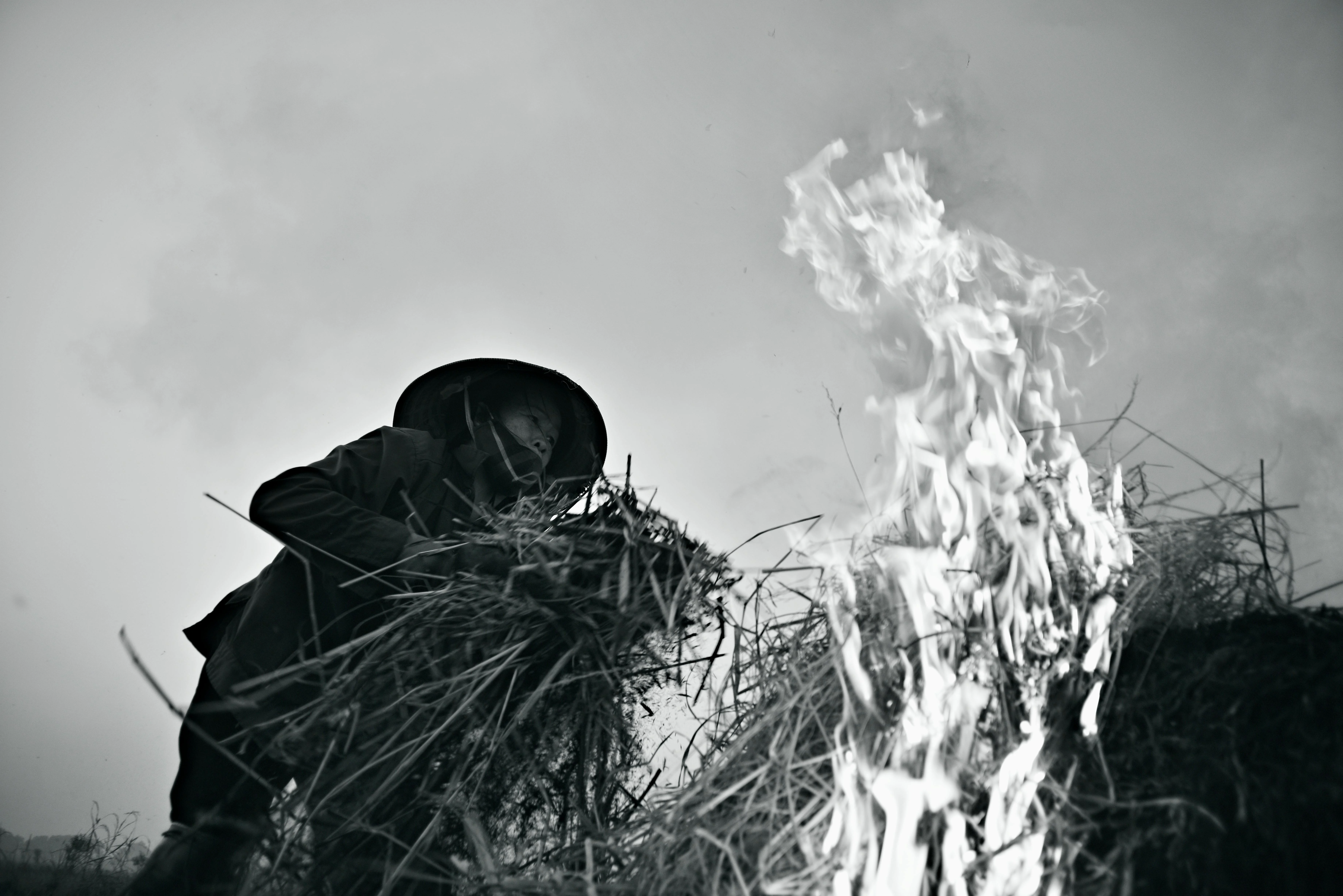 A farmer tending to a straw fire in an open field, captured in black and white