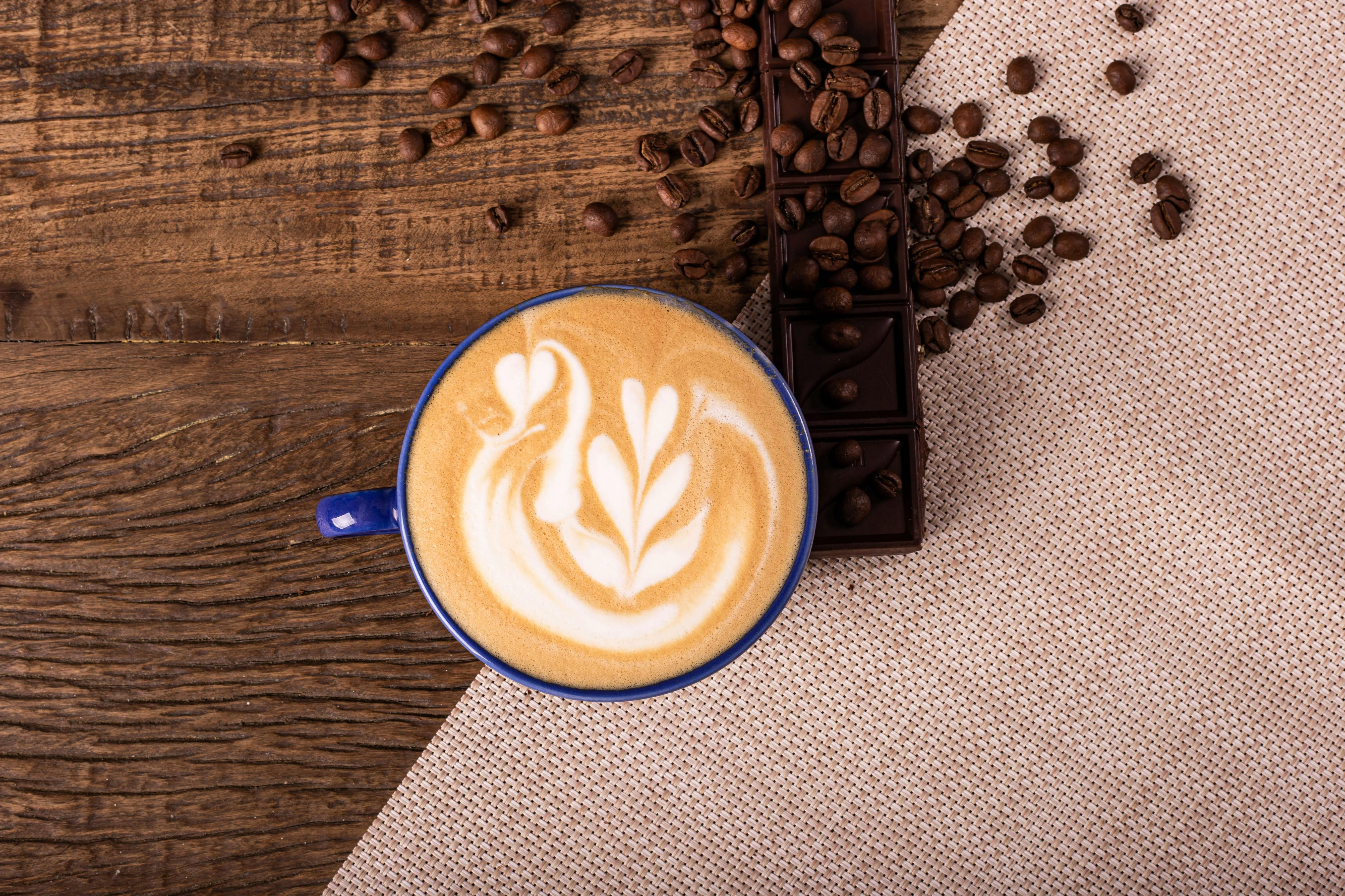 Overhead view of a latte with swan latte art, surrounded by coffee beans and chocolate on rustic wood.