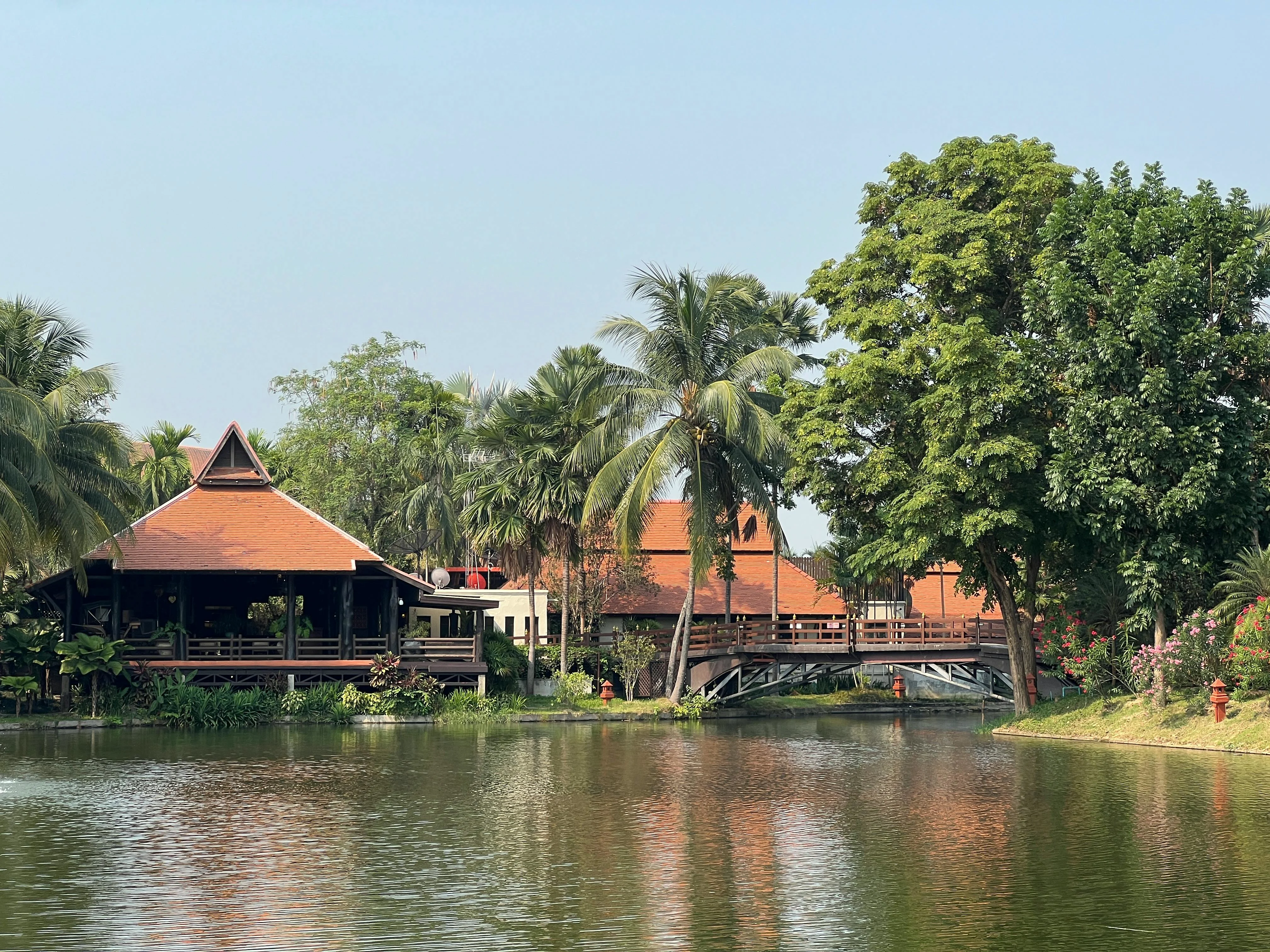 Tranquil scene of traditional Thai buildings by a river, surrounded by lush greenery.