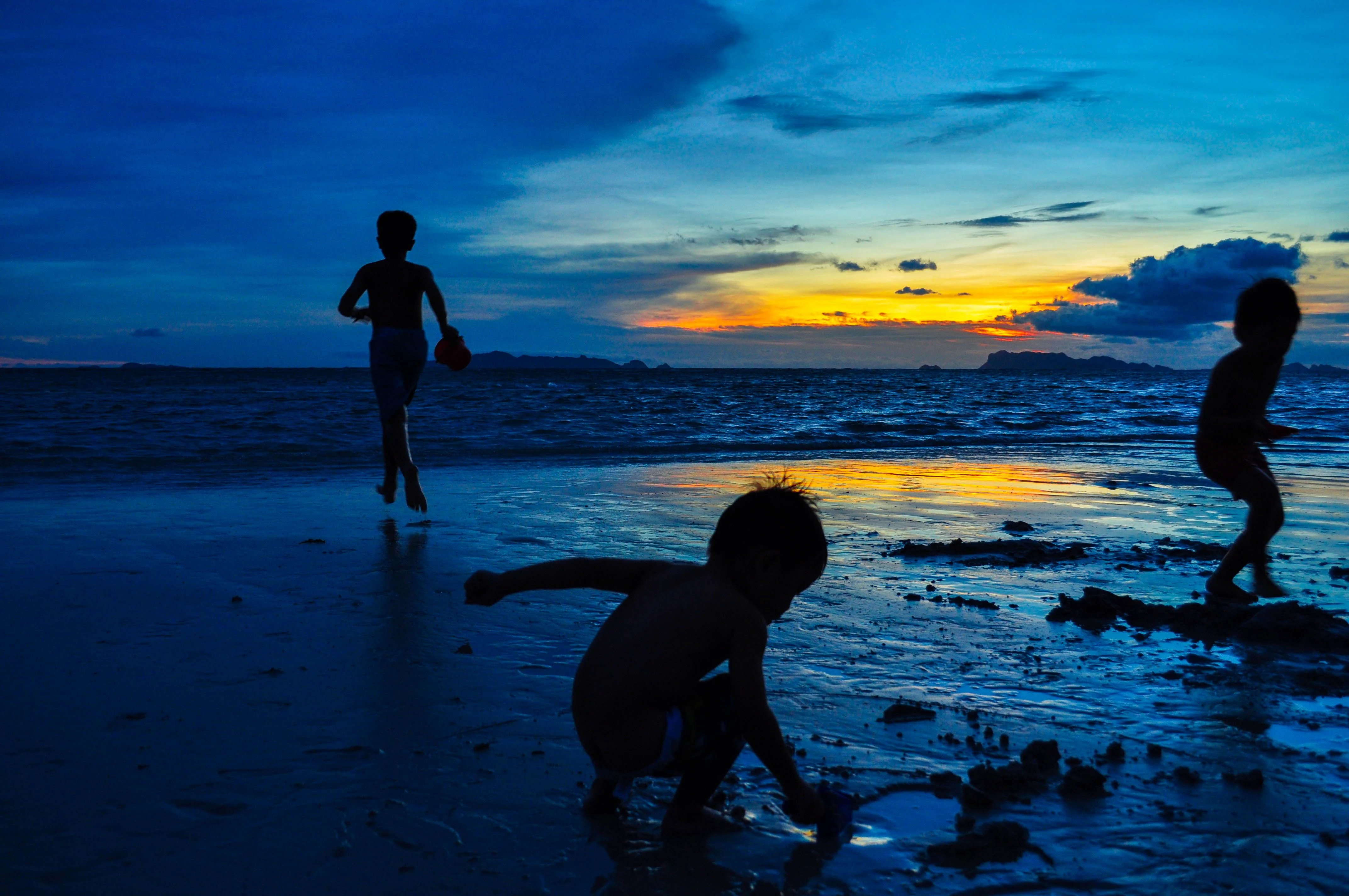 Silhouetted children enjoying a vibrant Koh Samui beach at sunset.