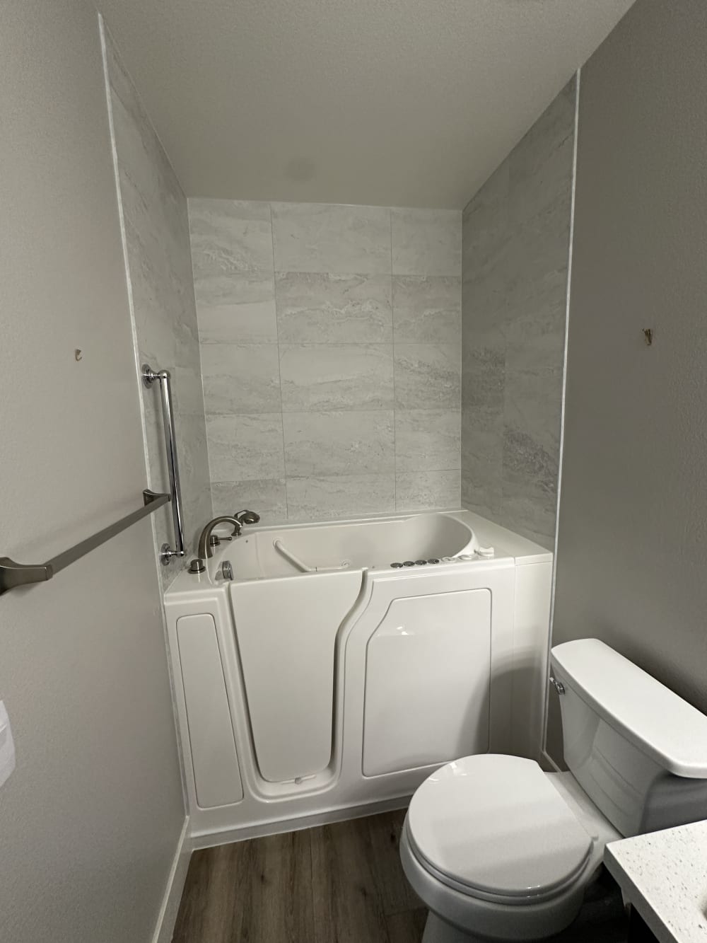 New walk-in safety tub with low-threshold door, grab bar, and grey marble-look surround after installation in Las Vegas by EZ Bath & Shower