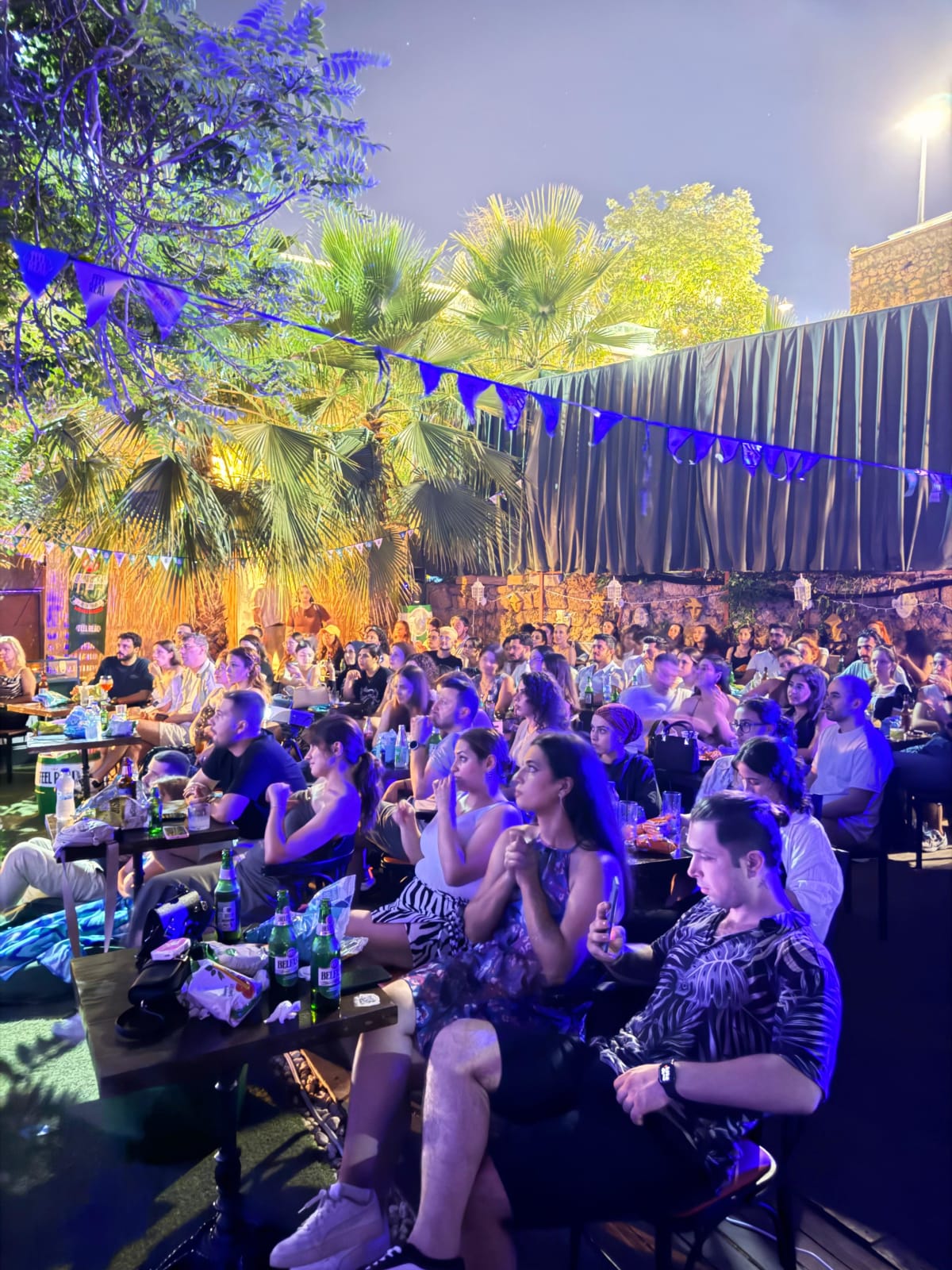 Outdoor cinema at night — guests at tables, palms and lights