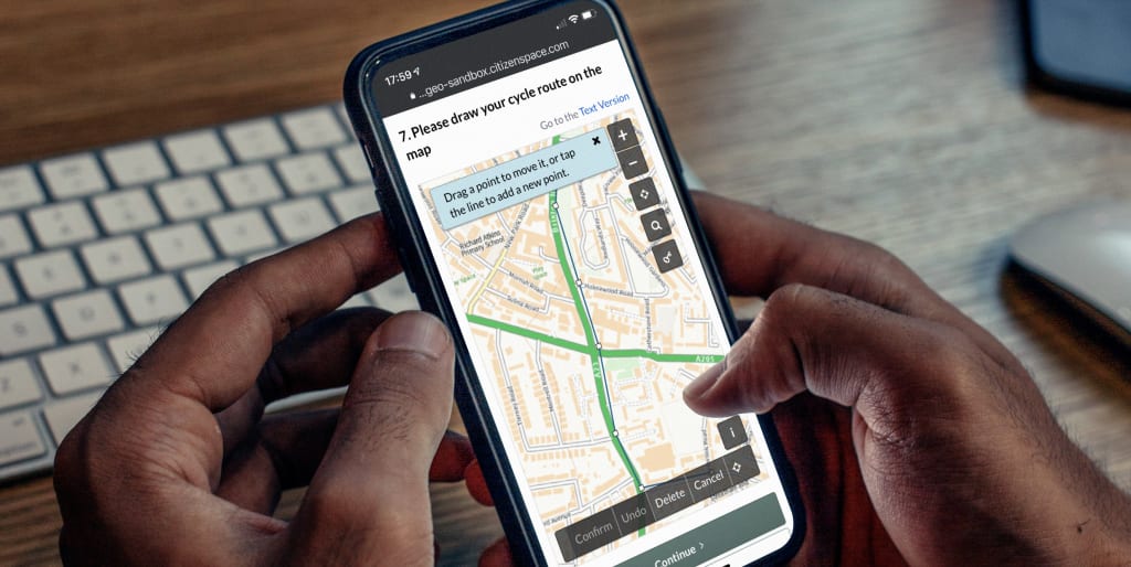 Hands holding a mobile phone. The screen displays Citizen Space Geospatial's 'draw line or route' feature, with a user-added route displaying over the base map