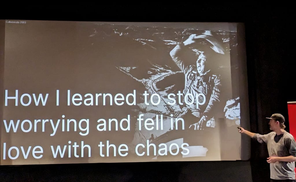 Designer Nils Bjorn presents in front of a large screen showing a slide that says 'How I learned to stop worrying and fell in love with the chaos'.