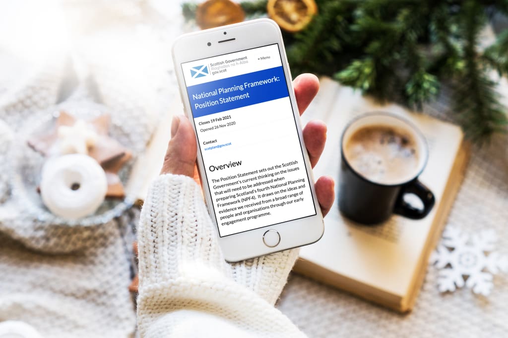 Woman's hand holding an iPhone; there are biscuits and coffee in the background. Displayed on the phone is Scottish Government's National Planning Framework: Position Statement consultation