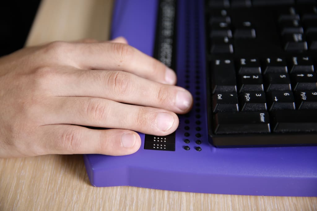 Blind person's hand using computer with braille computer display and a computer keyboard.