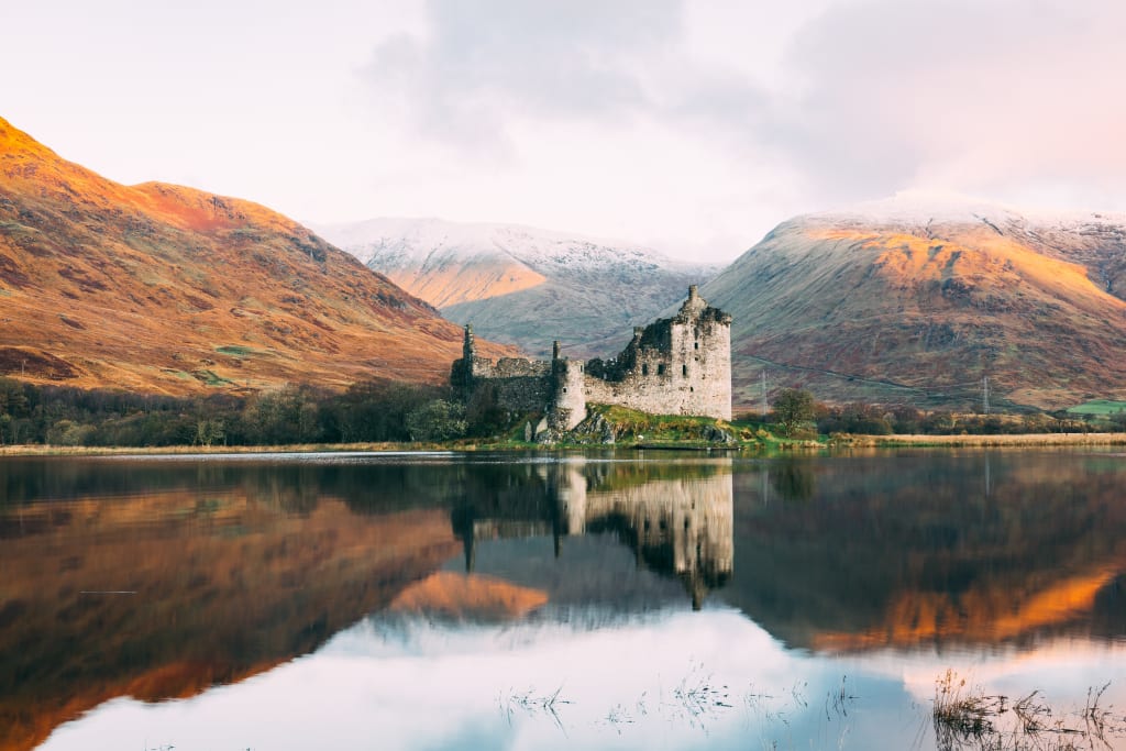 Remote Scottish castle ruin on the edge of a lake with mountains in the background
