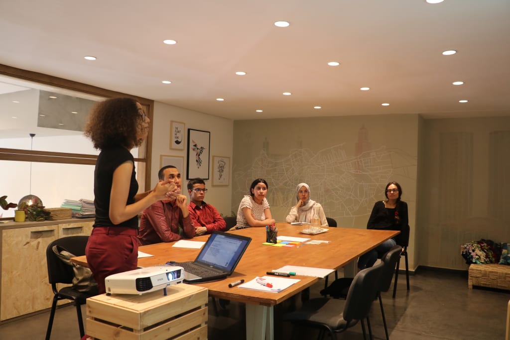 Image of a young woman leading a small boardroom style discussion.