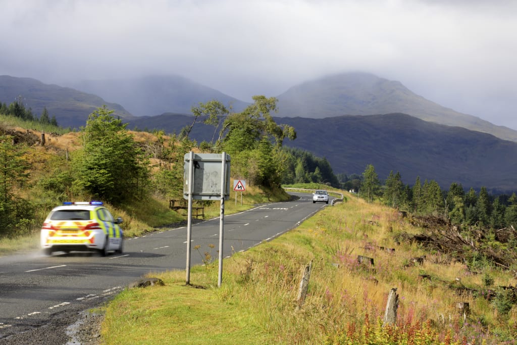 A police car drives through the mountainous landscape near Loch Awe, Scotland