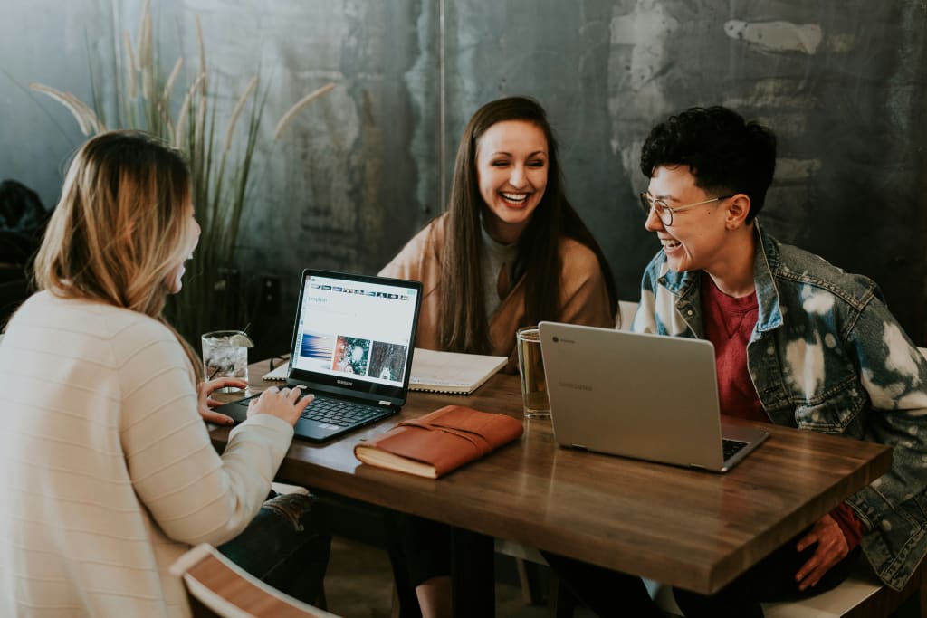 three millenials sat around a table with computers discussing