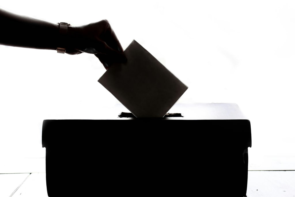 silhouette of a hand putting a ballot into a voting box