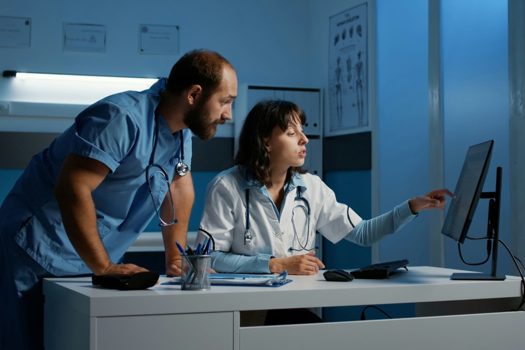 two healthcare professionals looking at computers at a desk