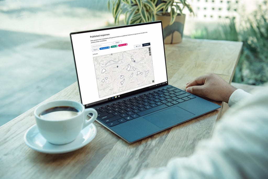 Laptop on a workbench next to a cup of coffee. Screen displays Citizen Space Geispatial's response publishing feature. Published responses are user-submitted shapes.